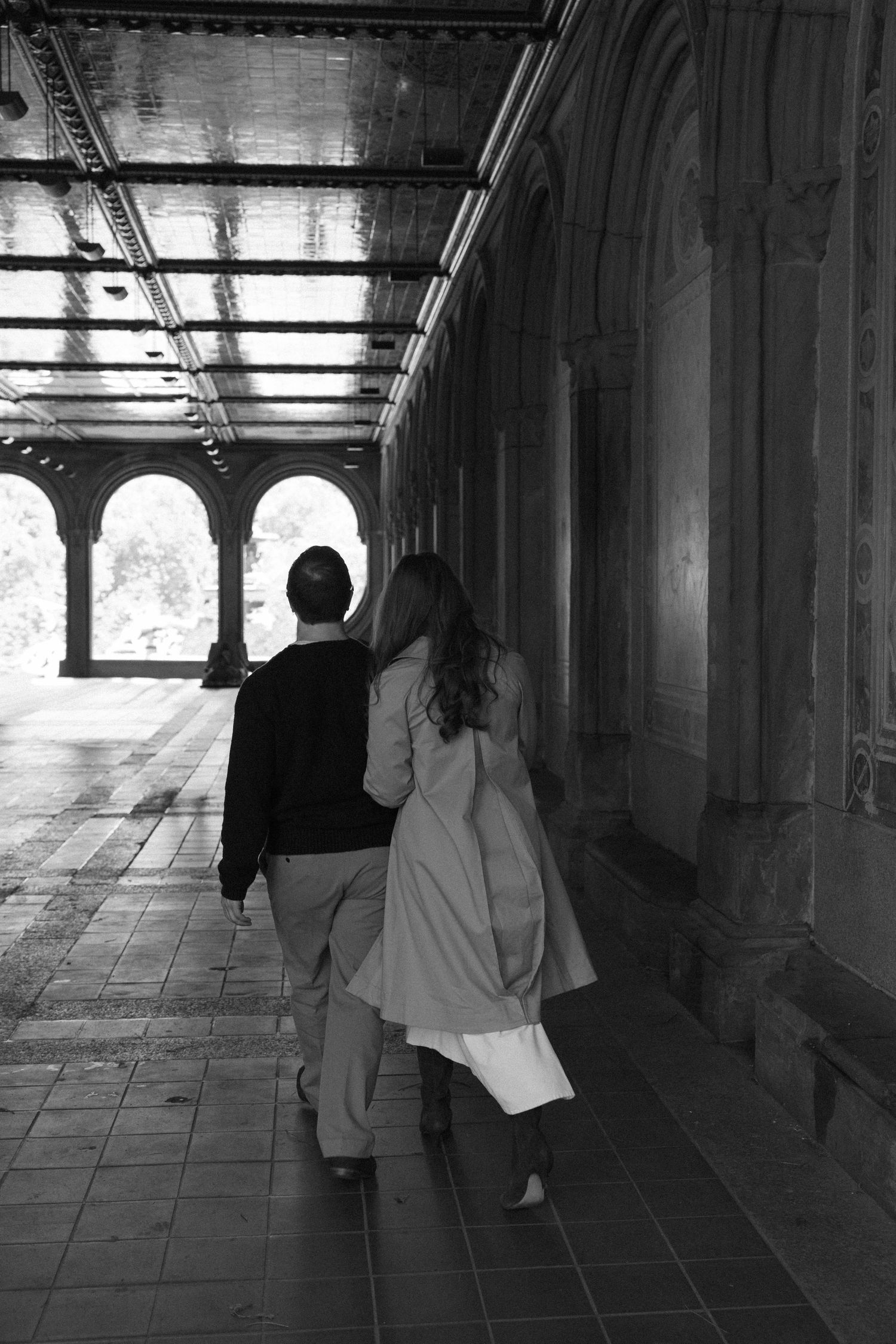 Black and white photo of couple walking hand in hand through Bethesda Terrace arcade in Central Park.