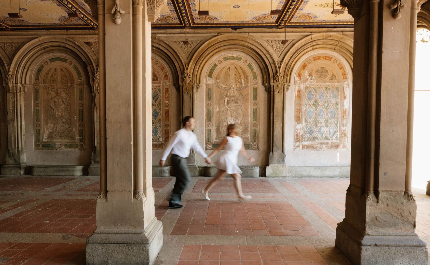 Couple holding hands running through ornate Bethesda Terrace arcade in Central Park, New York.