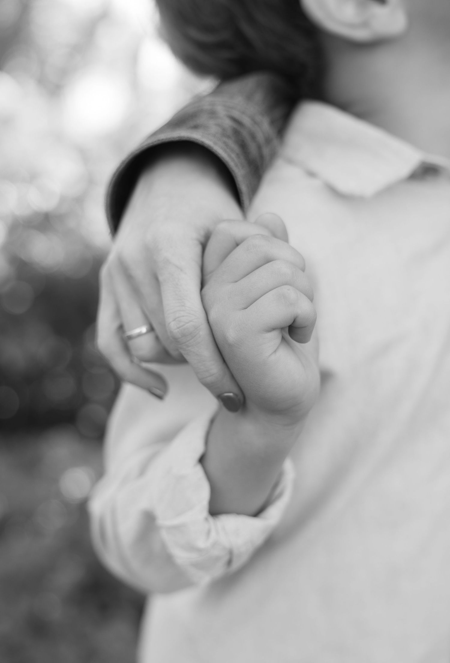 Black and white close-up of a parent's ringed hand gently holding a newborn baby's tiny fist.