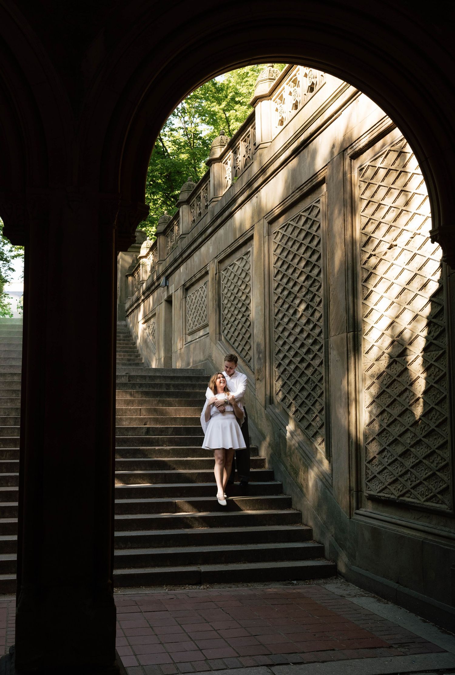 Couple embracing under stone arch at Bethesda Terrace stairway in Central Park, New York City.