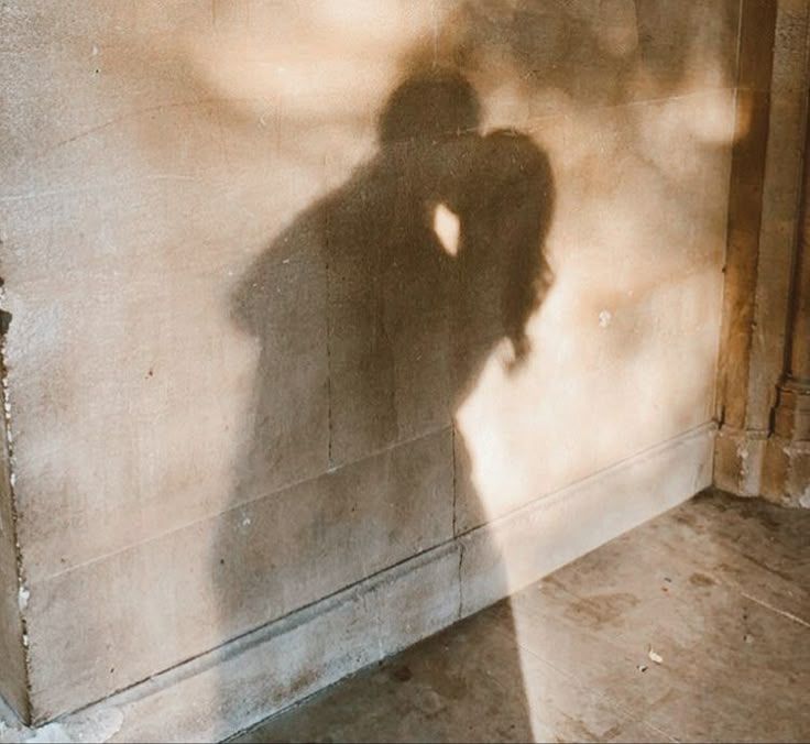 Romantic shadow of a couple kissing projected on a concrete wall in warm golden light.
