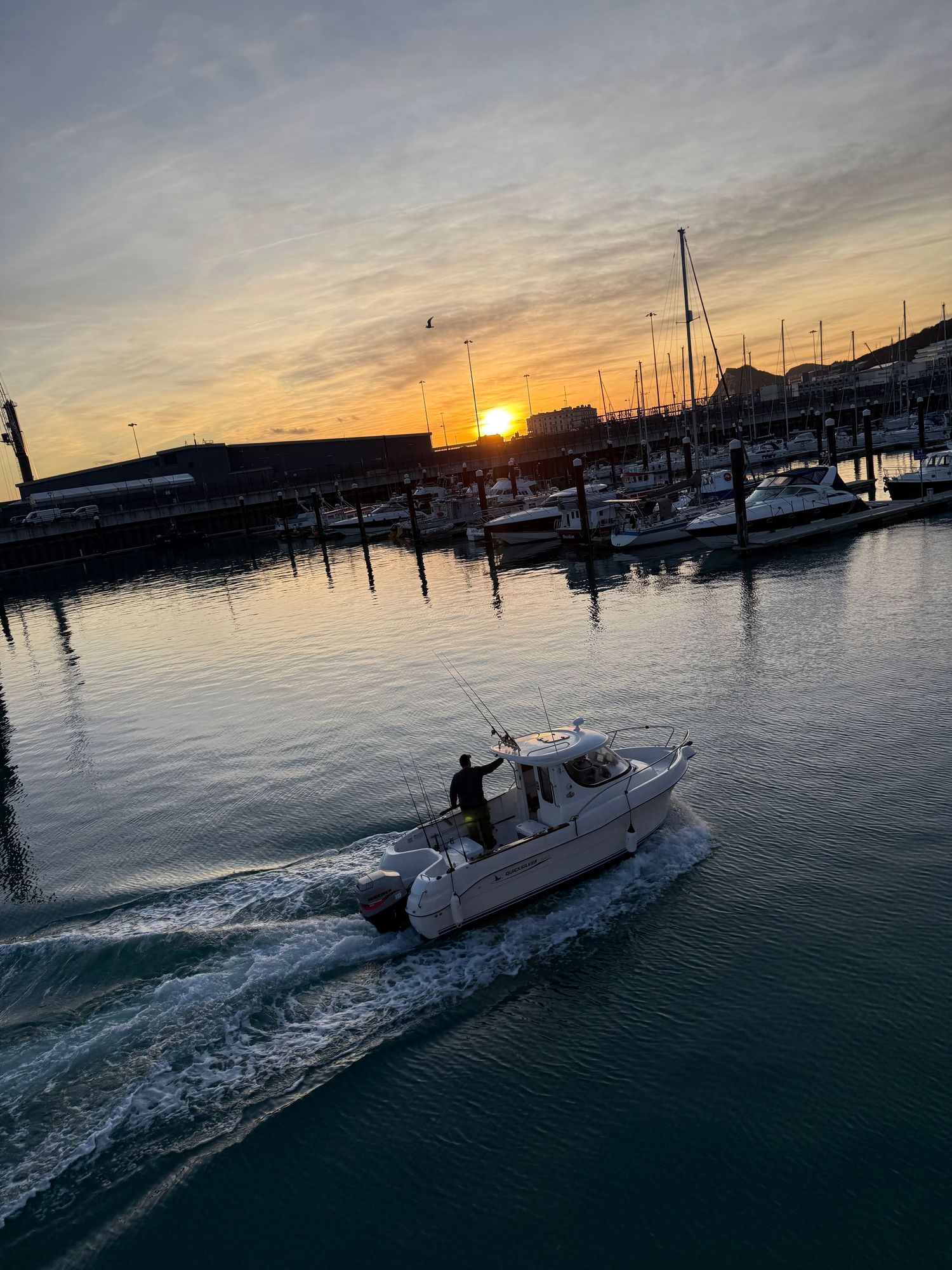 Sailboats cruising through harbor waters during a vibrant sunset.