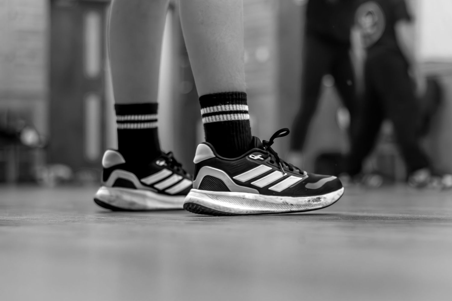 Close-up of Adidas sneakers with striped socks on a dance floor.