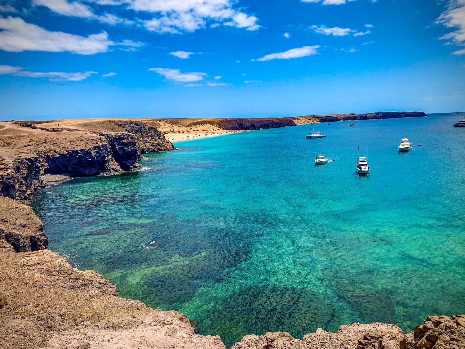 Stunning turquoise waters and rocky coastline with boats anchored in a pristine Mediterranean bay.