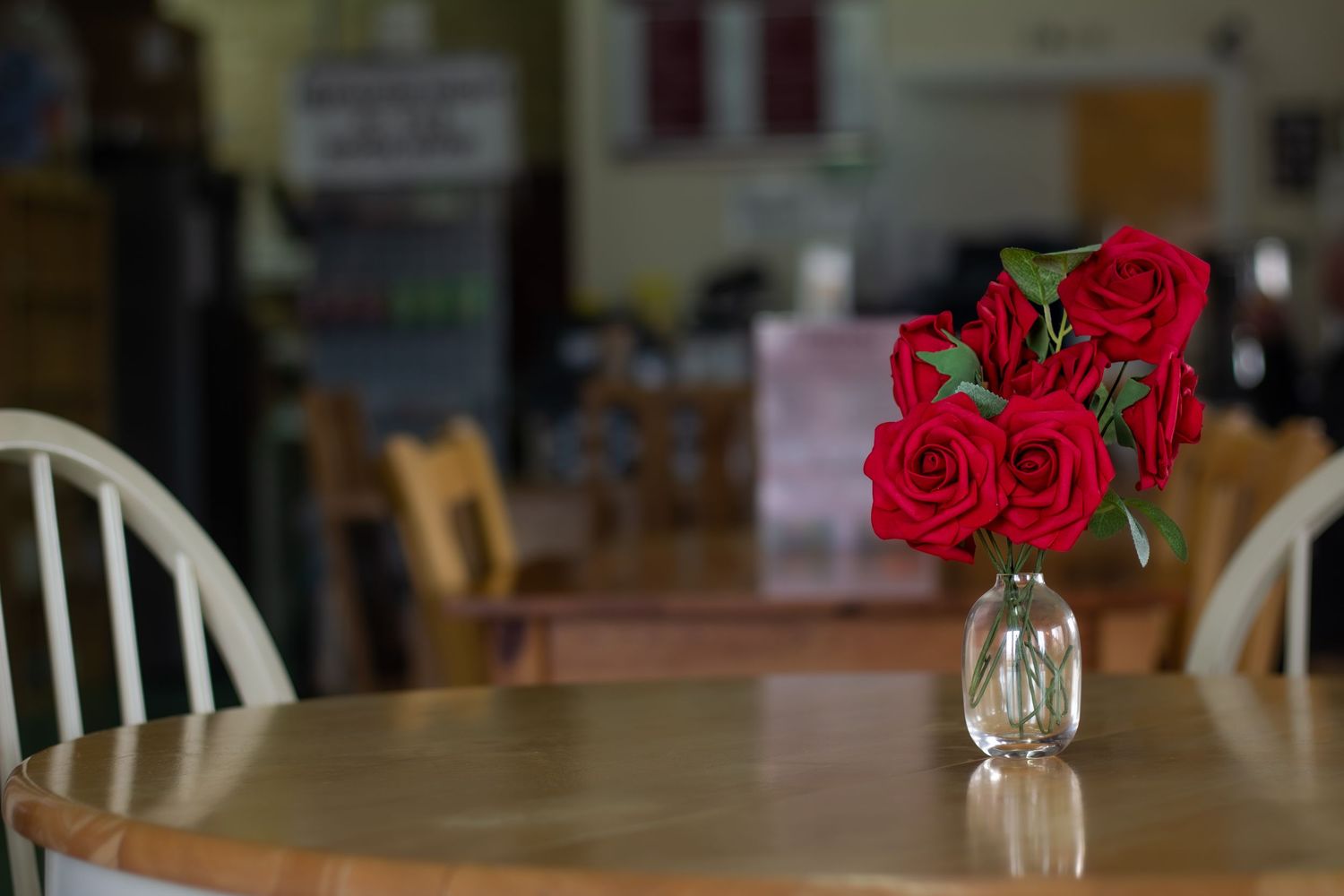 Red roses in clear glass vases decorate wooden tables in a rustic dining setting.