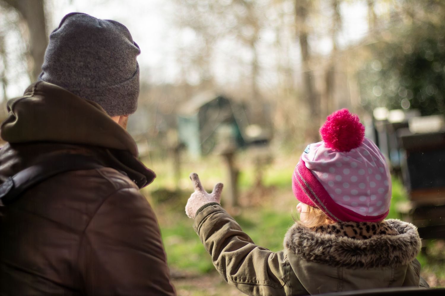 Two people in winter clothing pointing at something in a wooded setting.