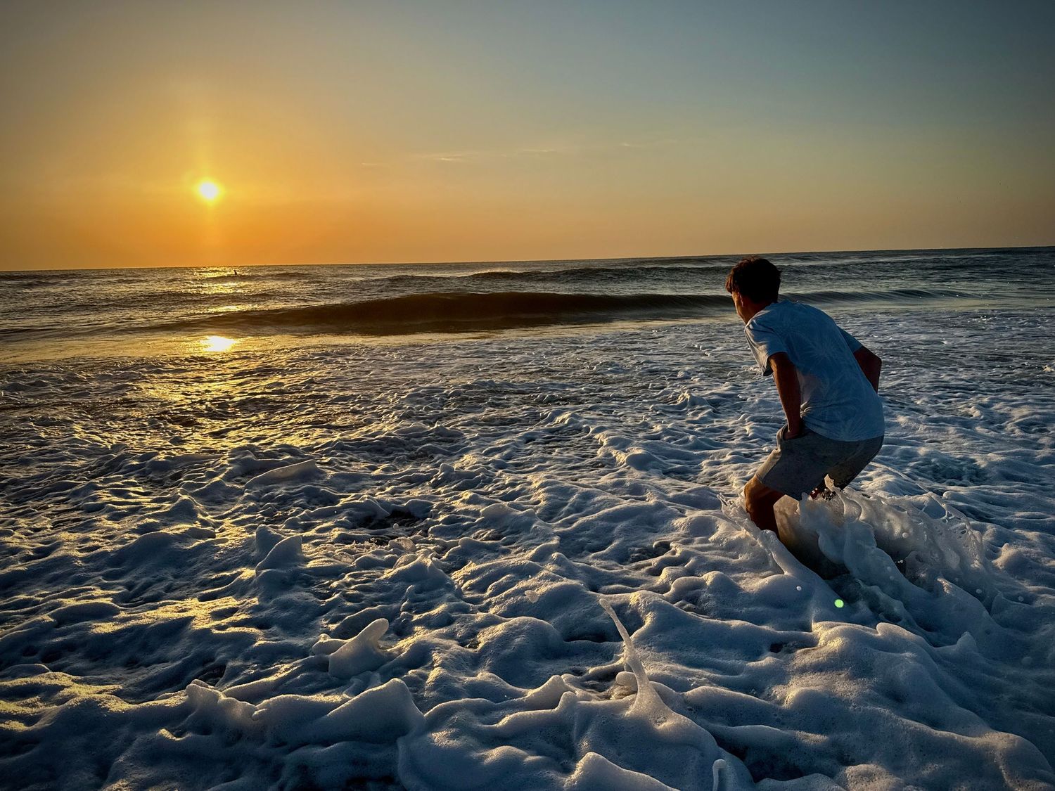 People playing in ocean waves at sunset with golden light reflecting off wet sand.
