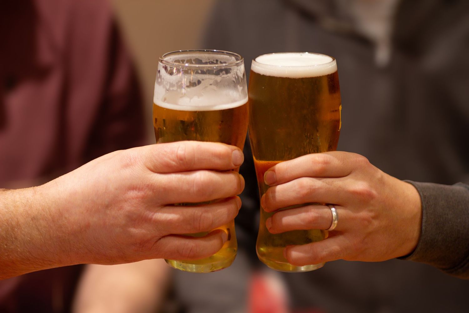Hands toasting with glasses of beer in a casual setting.