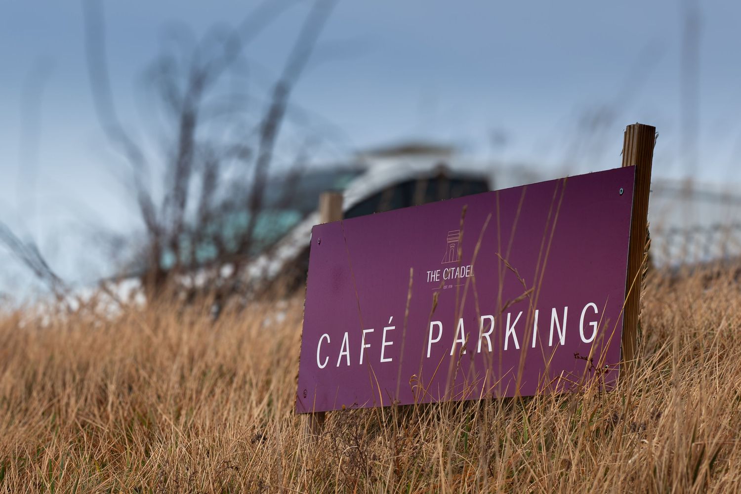 A rustic cafe parking sign stands against a backdrop of brown winter grass and cloudy sky.