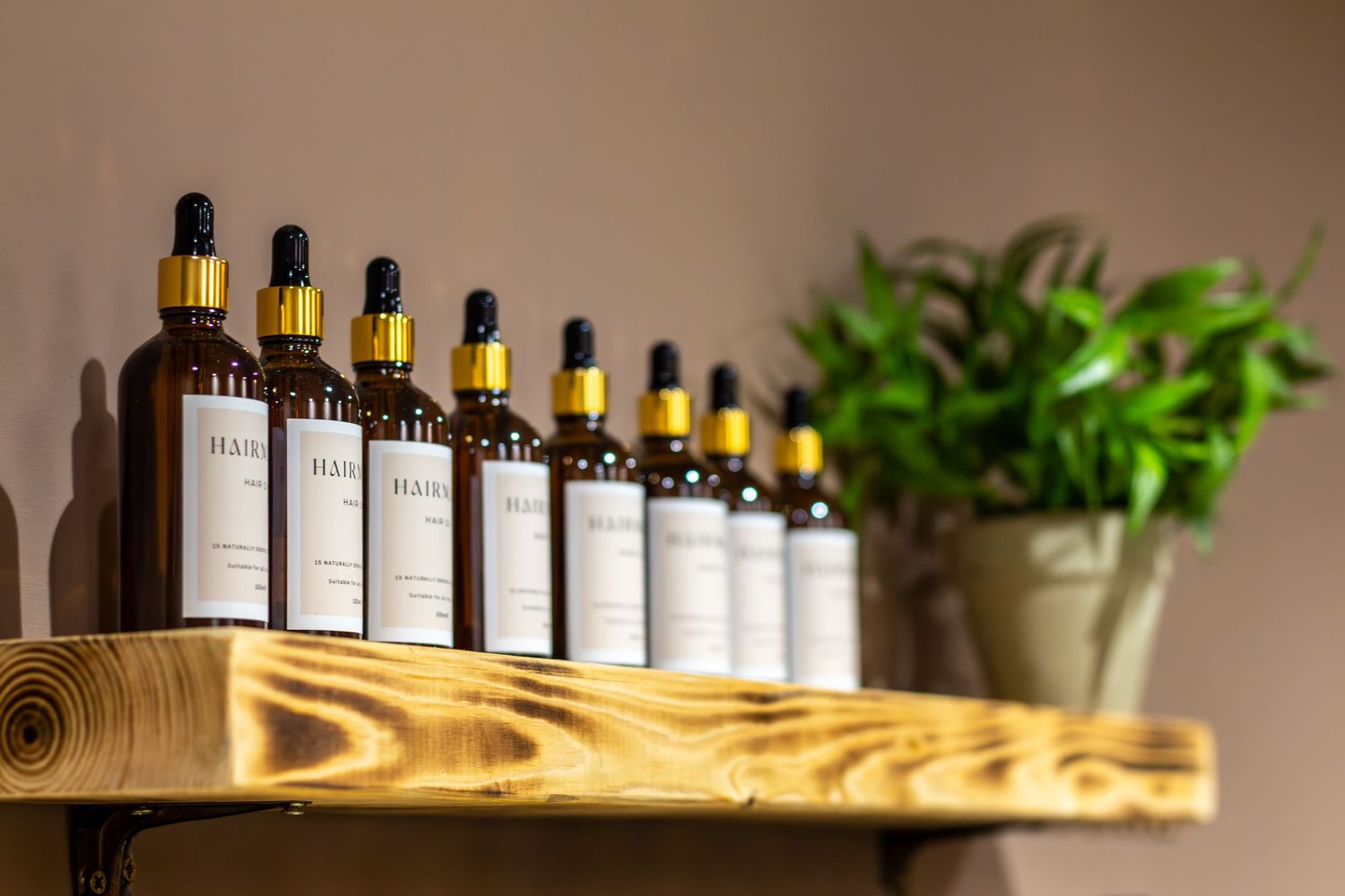 Row of essential oil bottles displayed on wooden shelving with green plants.