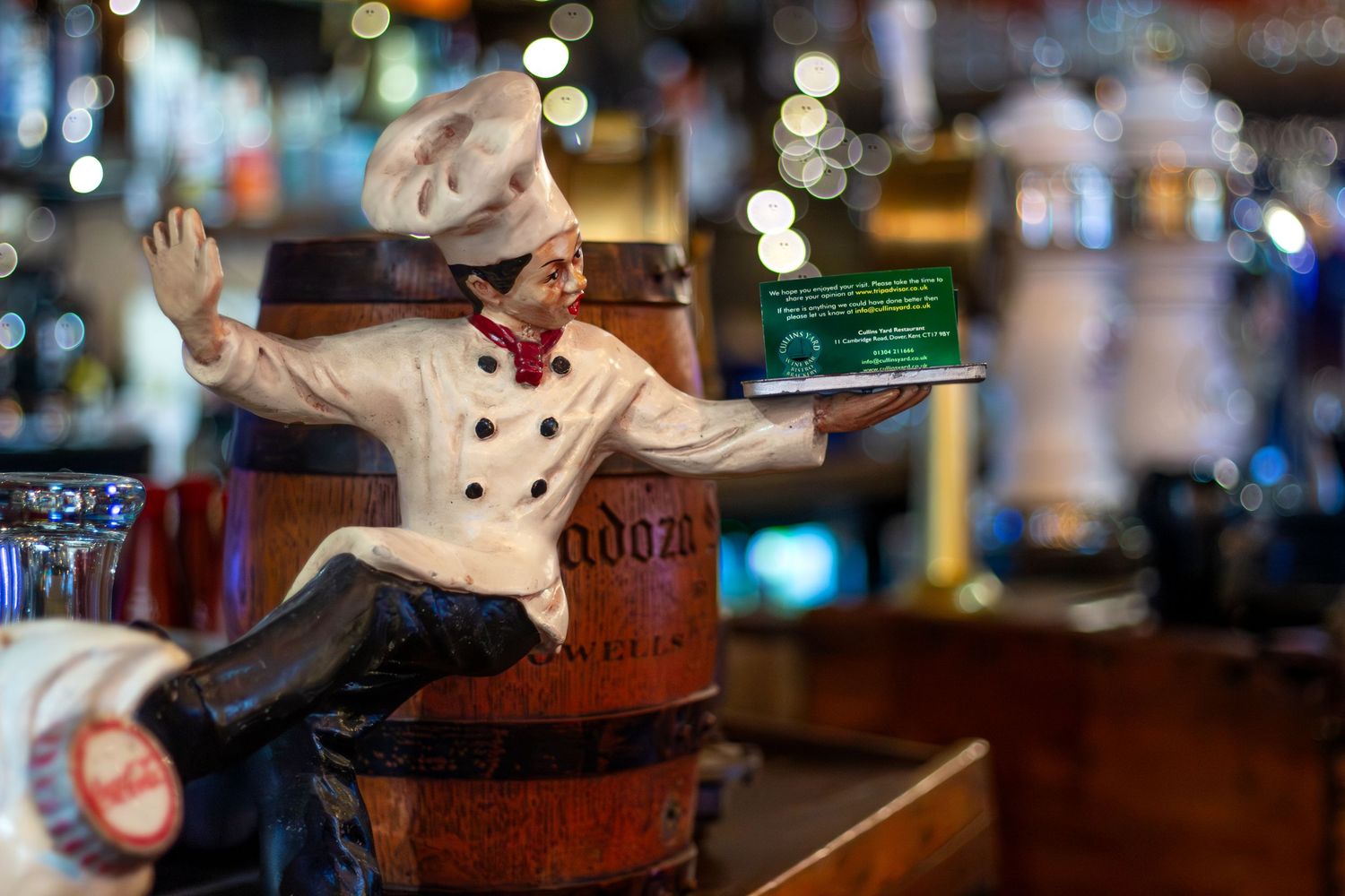 Decorative chef figurines displayed on wooden barrels in bar setting.