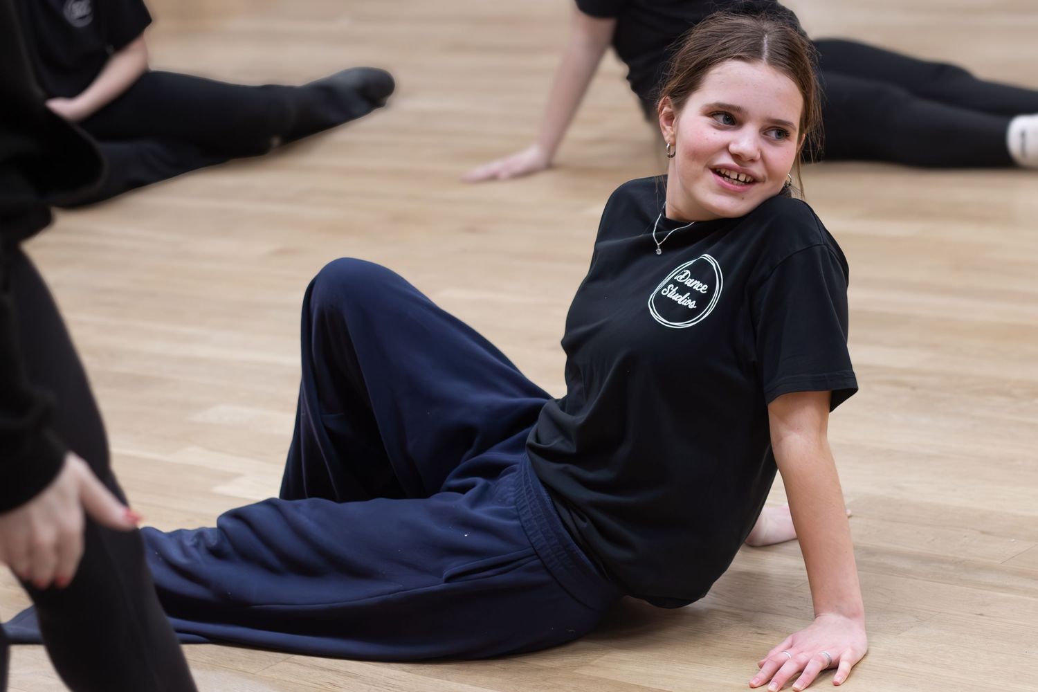 Dancers stretching and warming up on a wooden floor in a dance studio.