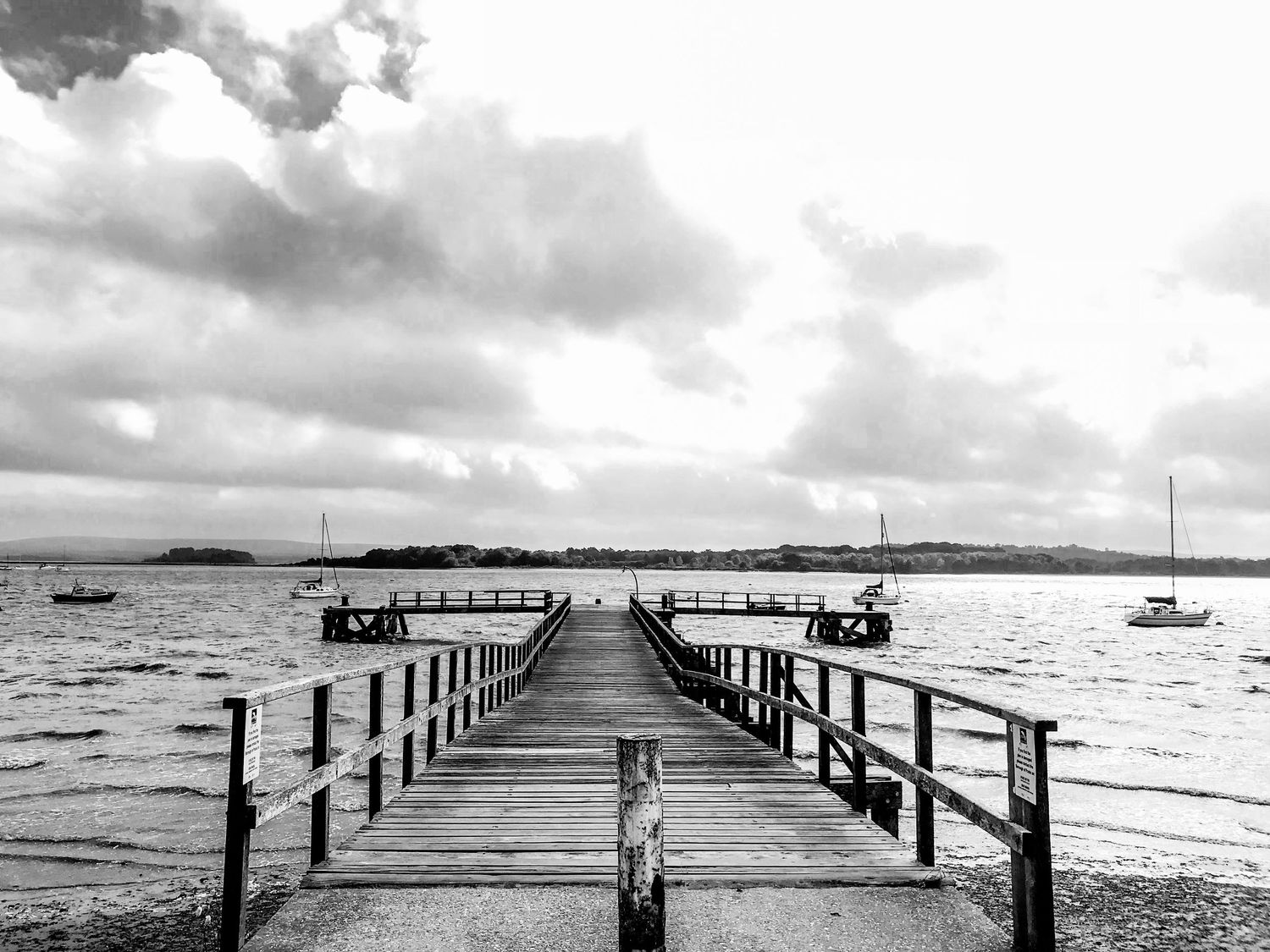Long wooden pier stretches into calm ocean waters under dramatic cloudy sky.
