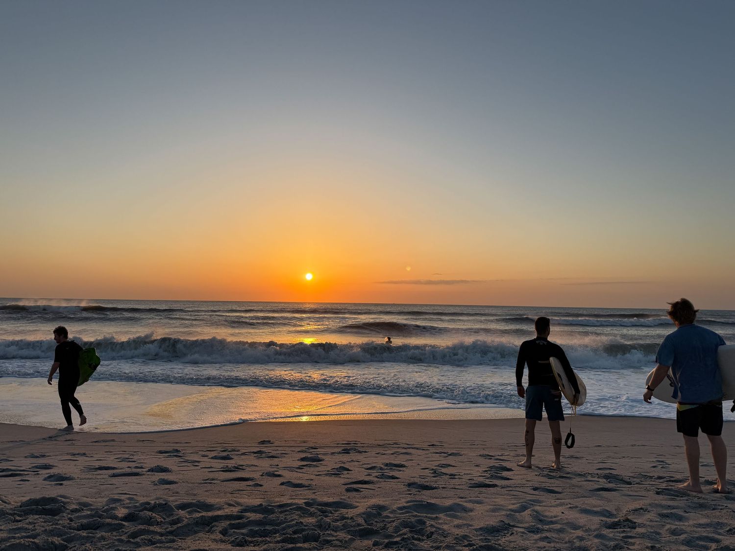 Silhouettes of people walking on beach during vibrant orange sunset over ocean.