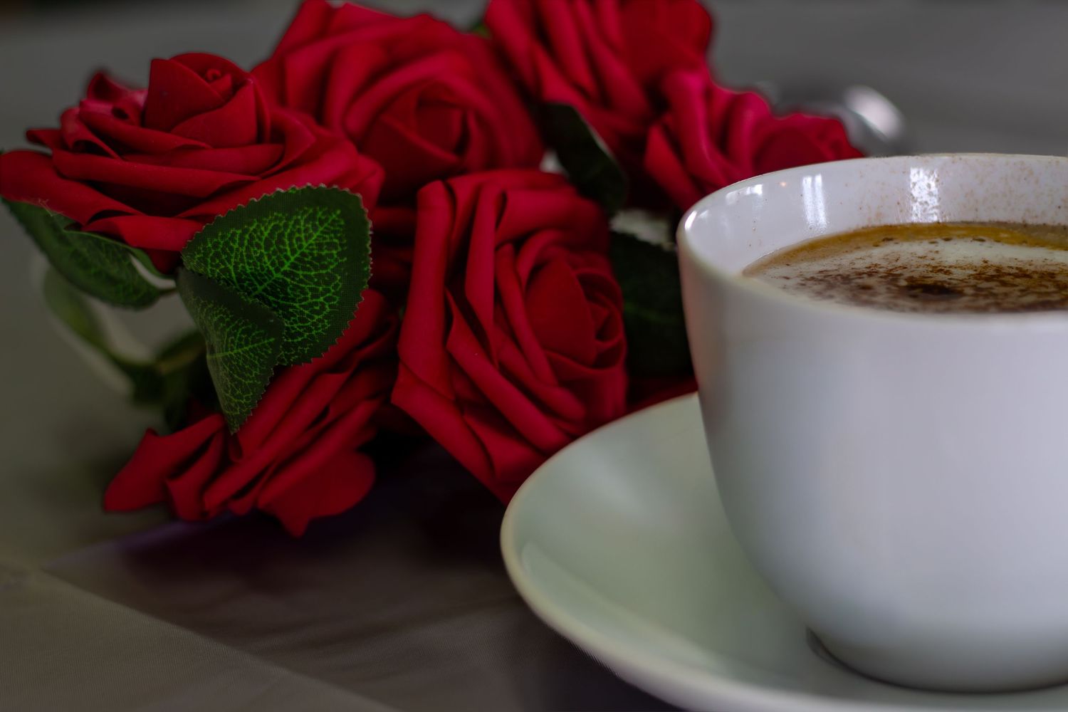 Red roses and coffee cups arranged on a white table setting.