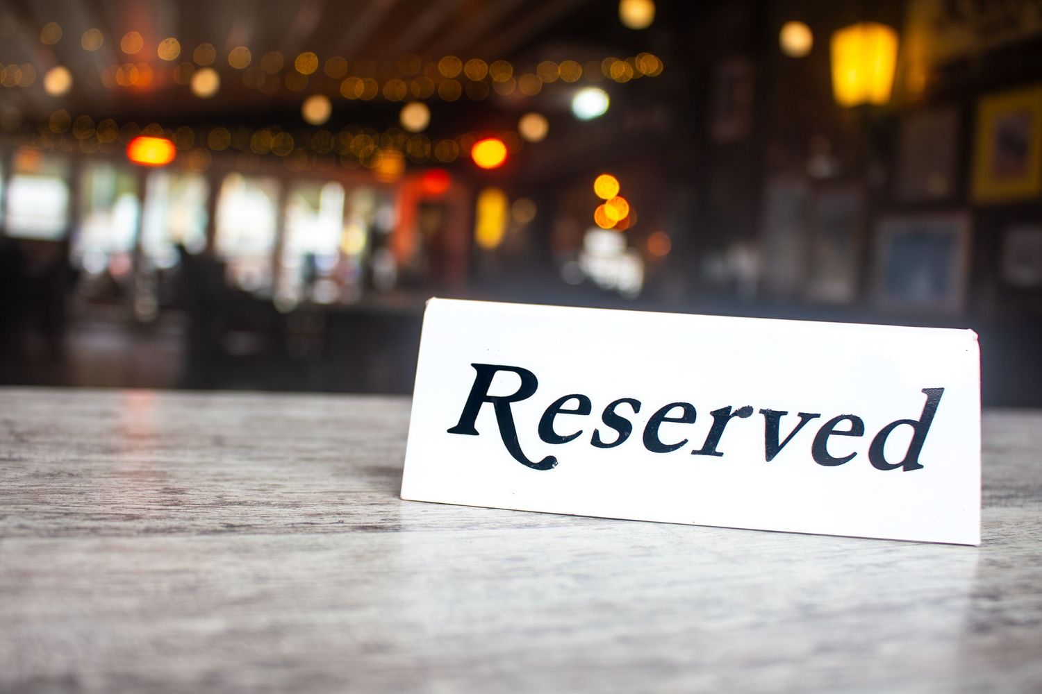 Reserved sign on wooden table with blurred restaurant lighting in background.