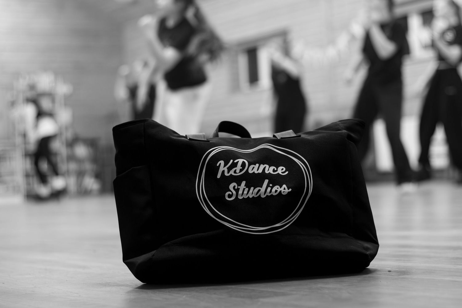 Dance studio gear bags lined up in black and white on a wooden floor.