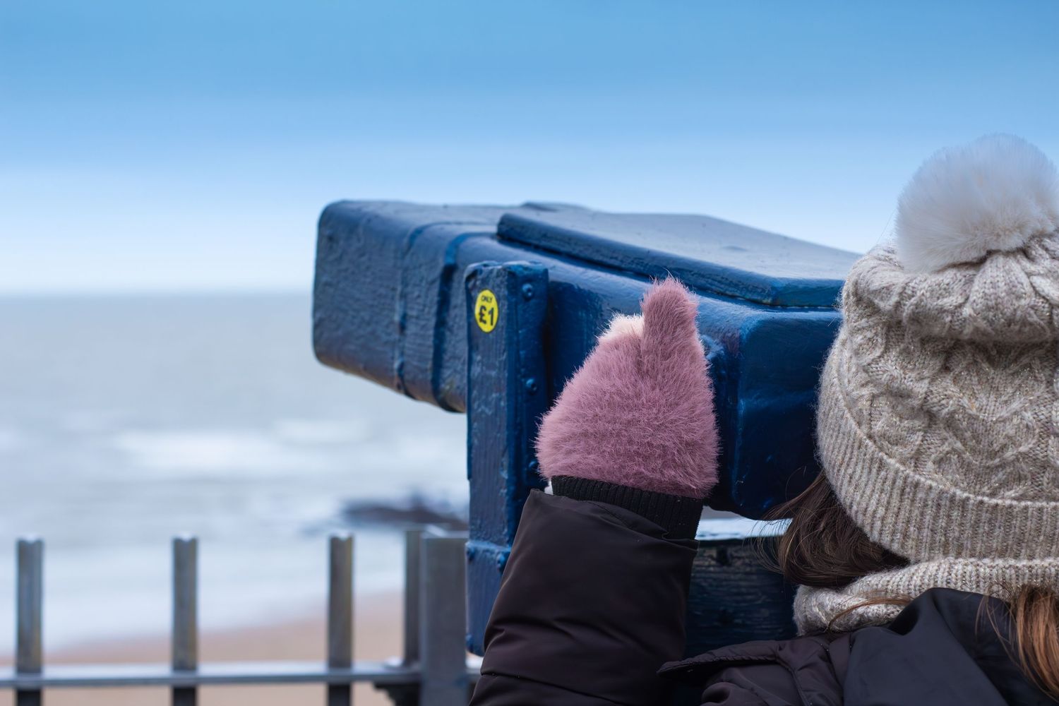 Row of binoculars mounted on observation deck railing against blue sky.