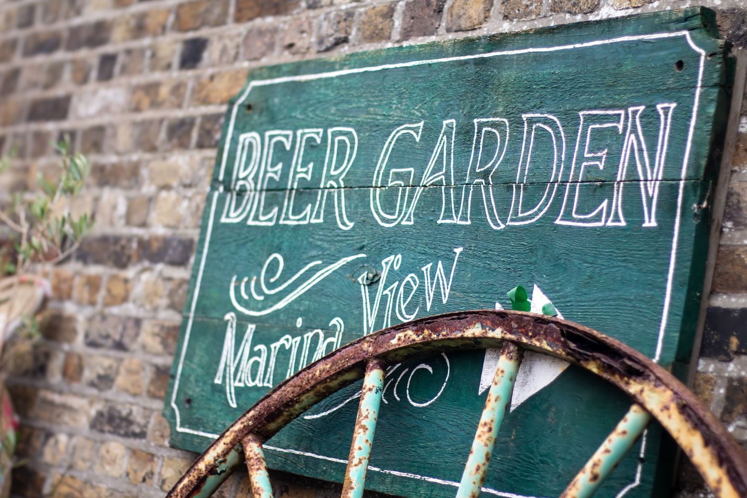 Rustic beer garden sign made with wooden wheel against weathered brick wall.