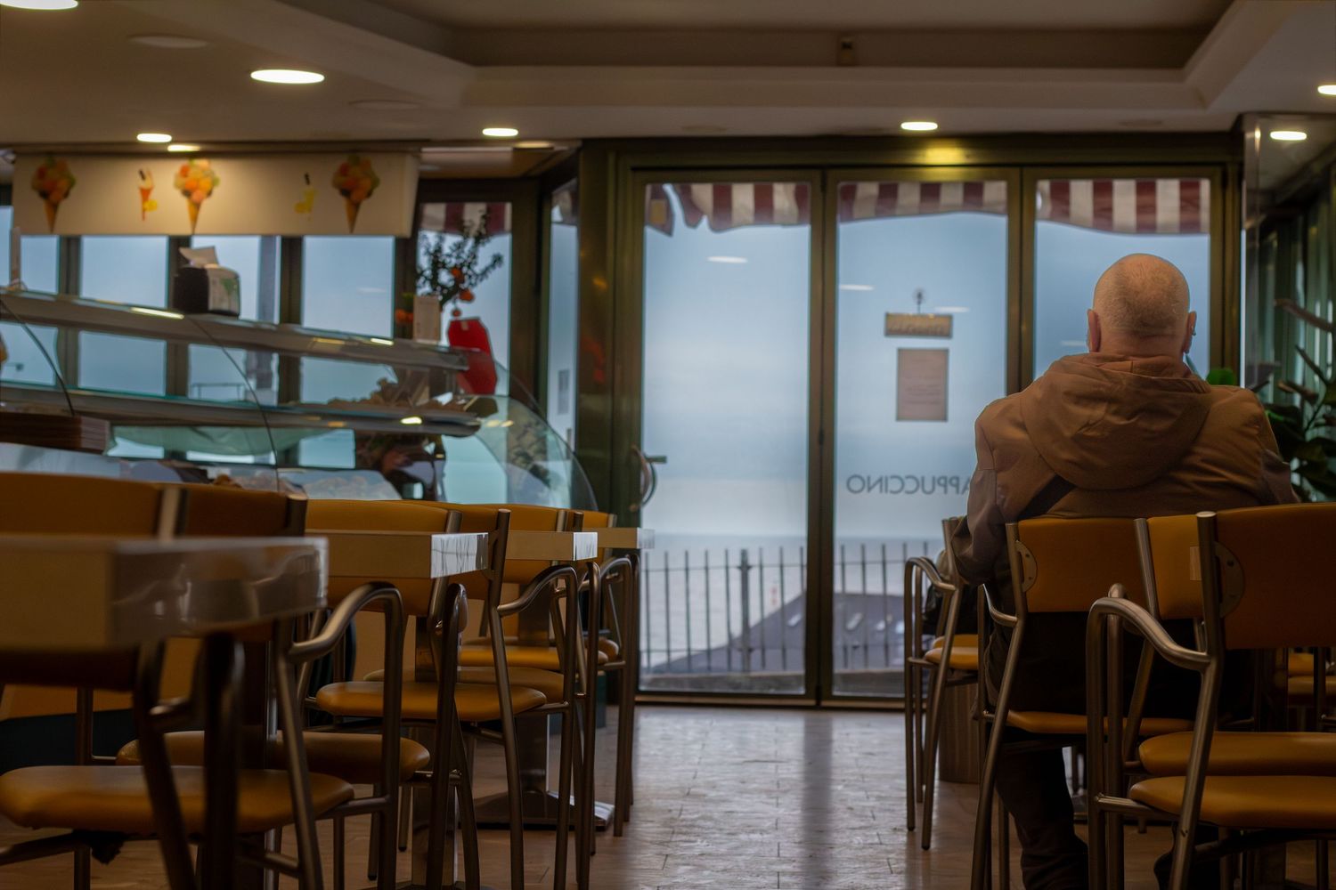 A bright cafe interior with wooden tables and chairs facing large windows with water views.
