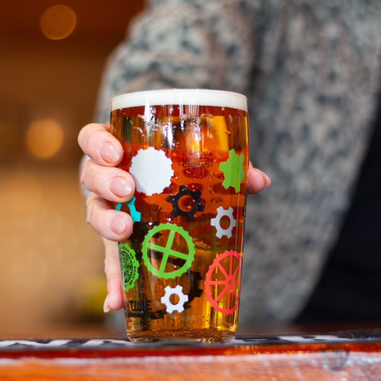 Glass of amber beer with colorful gear pattern designs on the side.