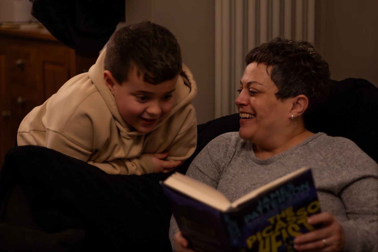 Two people sharing a laugh while reading a book together on a couch.