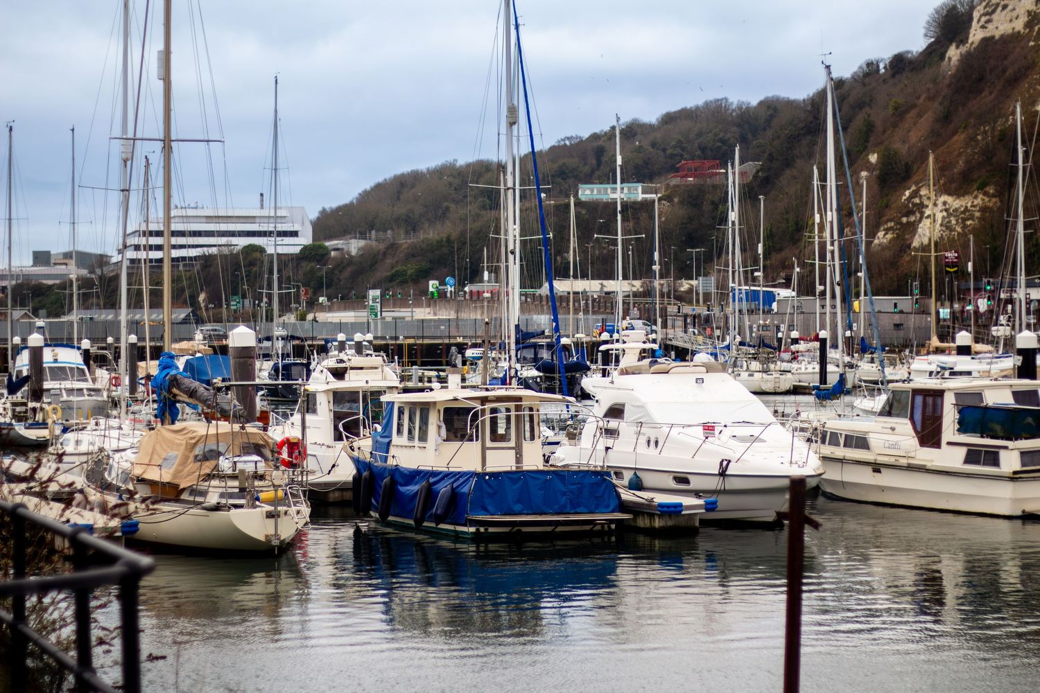Marina filled with sailboats and yachts moored along the waterfront on a calm day.