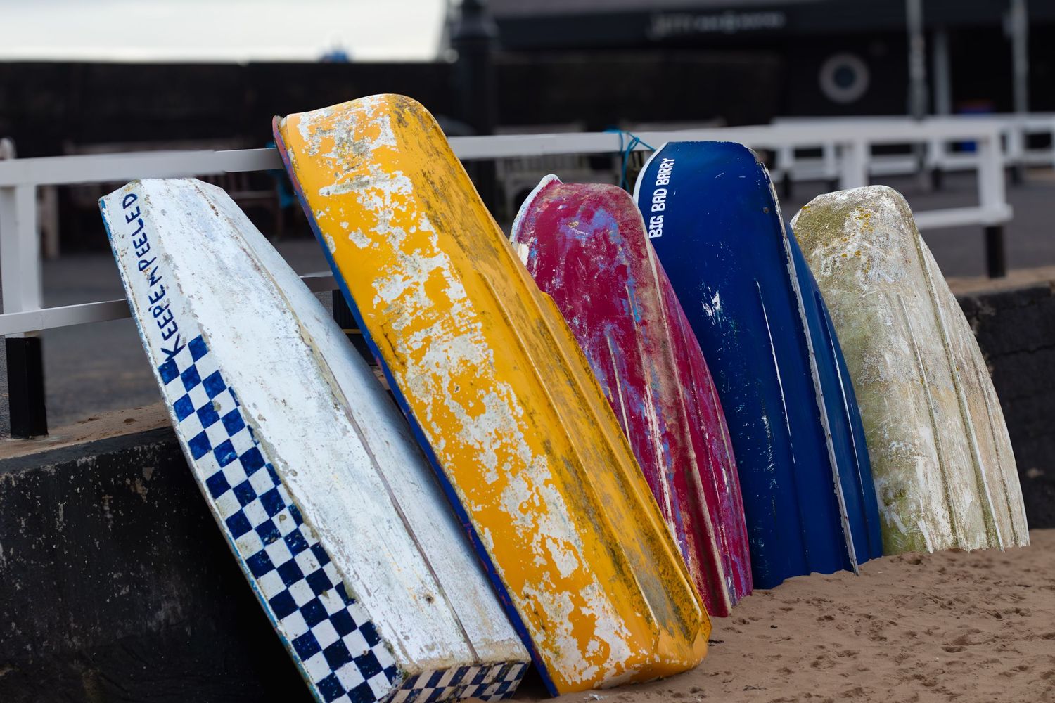 Row of weathered surfboards in various colors leaning against a wall.