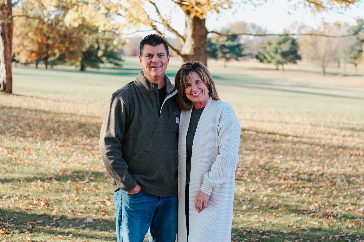 Smiling couple posing together outdoors under a large tree on a sunny autumn day. Zionsville family photographer Regan Nichalson Creative