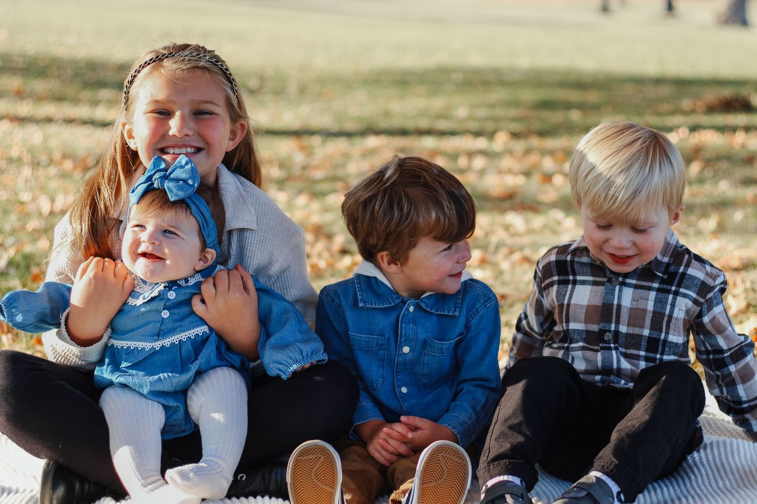 Four young siblings sitting together on a blanket in an autumn outdoor Zionsville family photographer Regan Nichalson Creative
