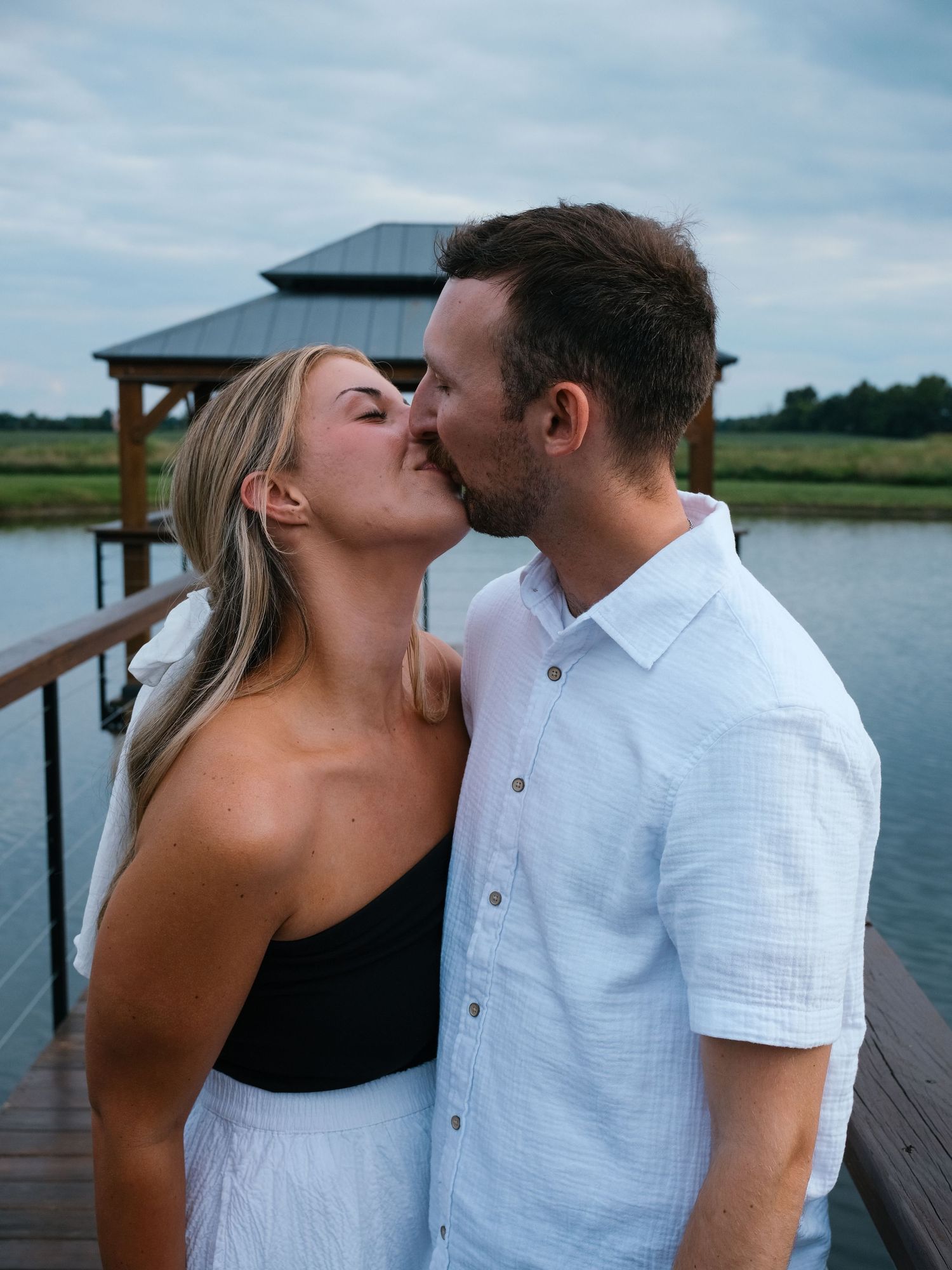 Couple sharing a tender kiss on wooden dock with gazebo and calm lake Hamilton County couples photographer Regan Nichalson Creative