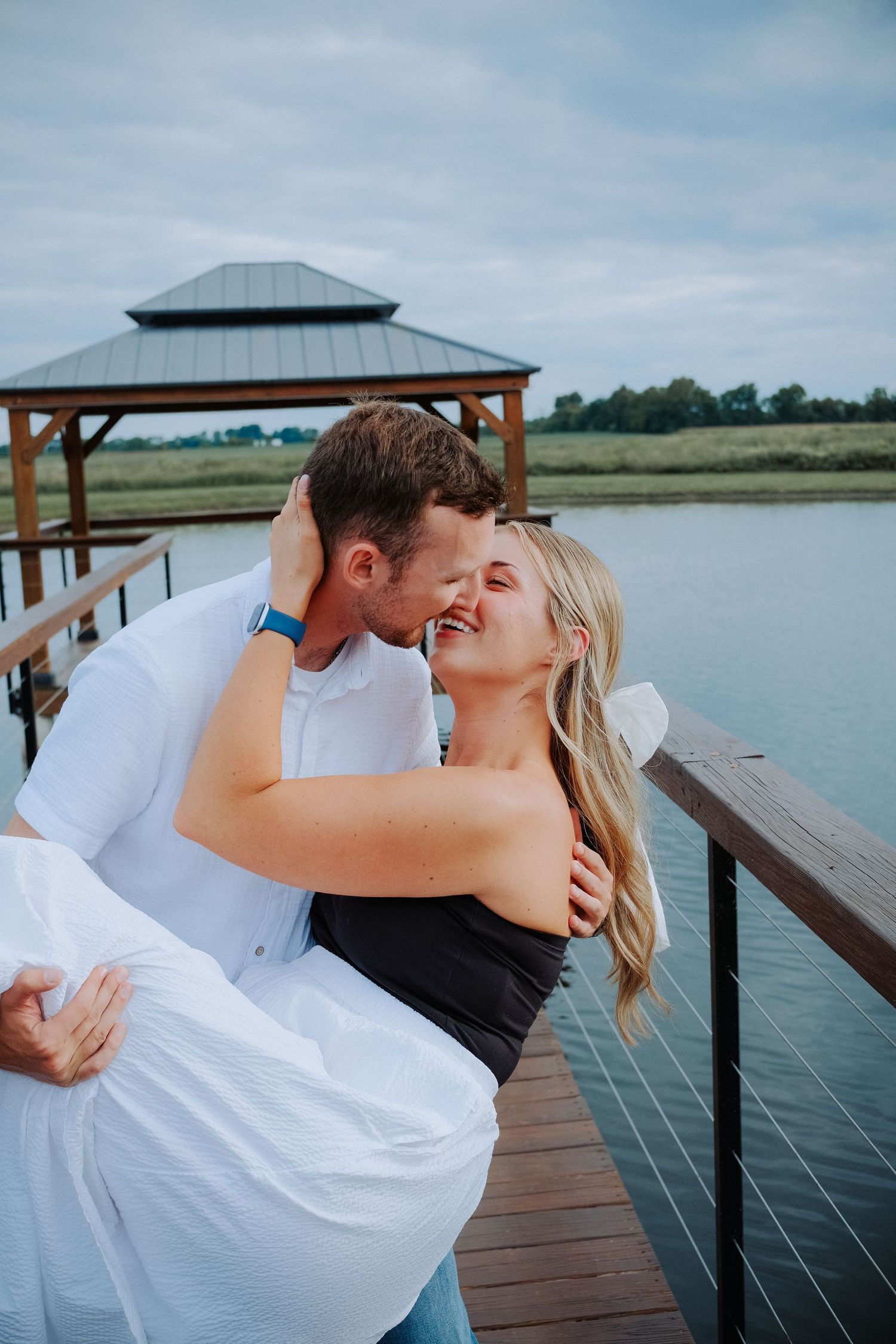 Couple sharing a romantic dip kiss on a wooden dock overlooking a serene lake Hamilton County couples photographer Regan Nichalson Creative