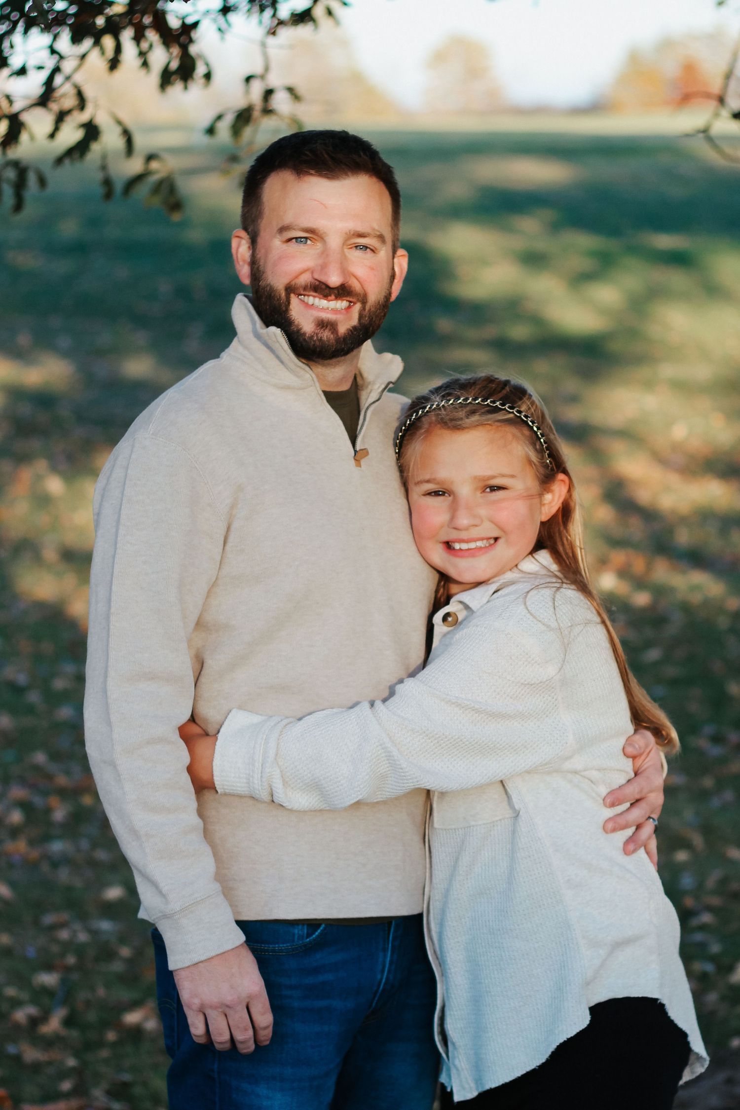 Smiling father hugging his young daughter outdoors in a sunny autumn park Zionsville family photographer Regan Nichalson Creative