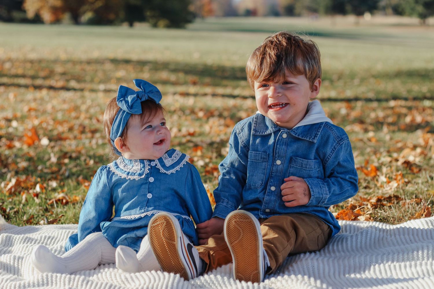 Two young toddlers in matching denim outfits sitting together on a white blanket Zionsville family photographer Regan Nichalson Creative