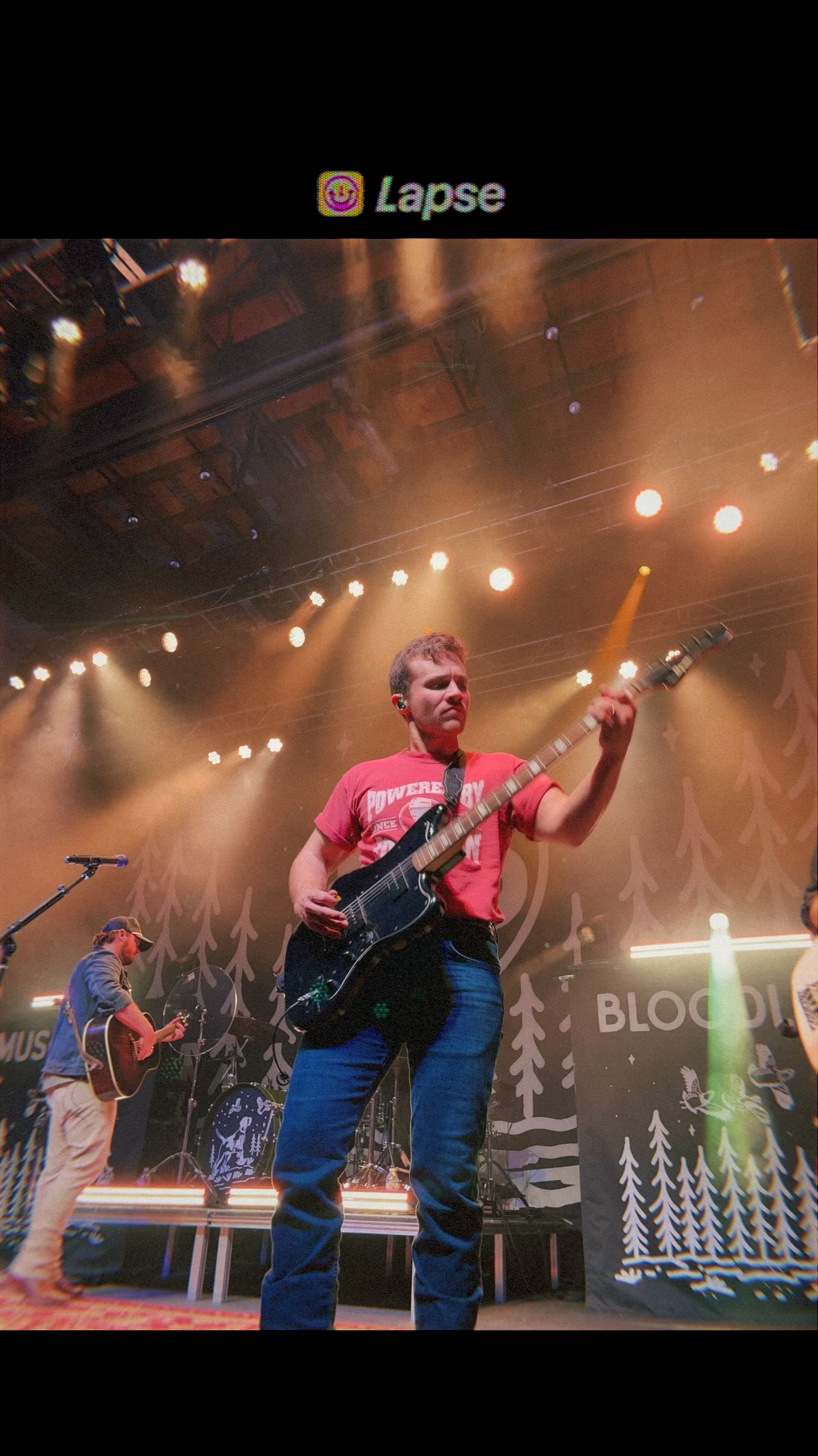 Guitarist in pink shirt performing on a lit concert stage with overhead lighting, Carmel family photographer Regan Nichalson Creative