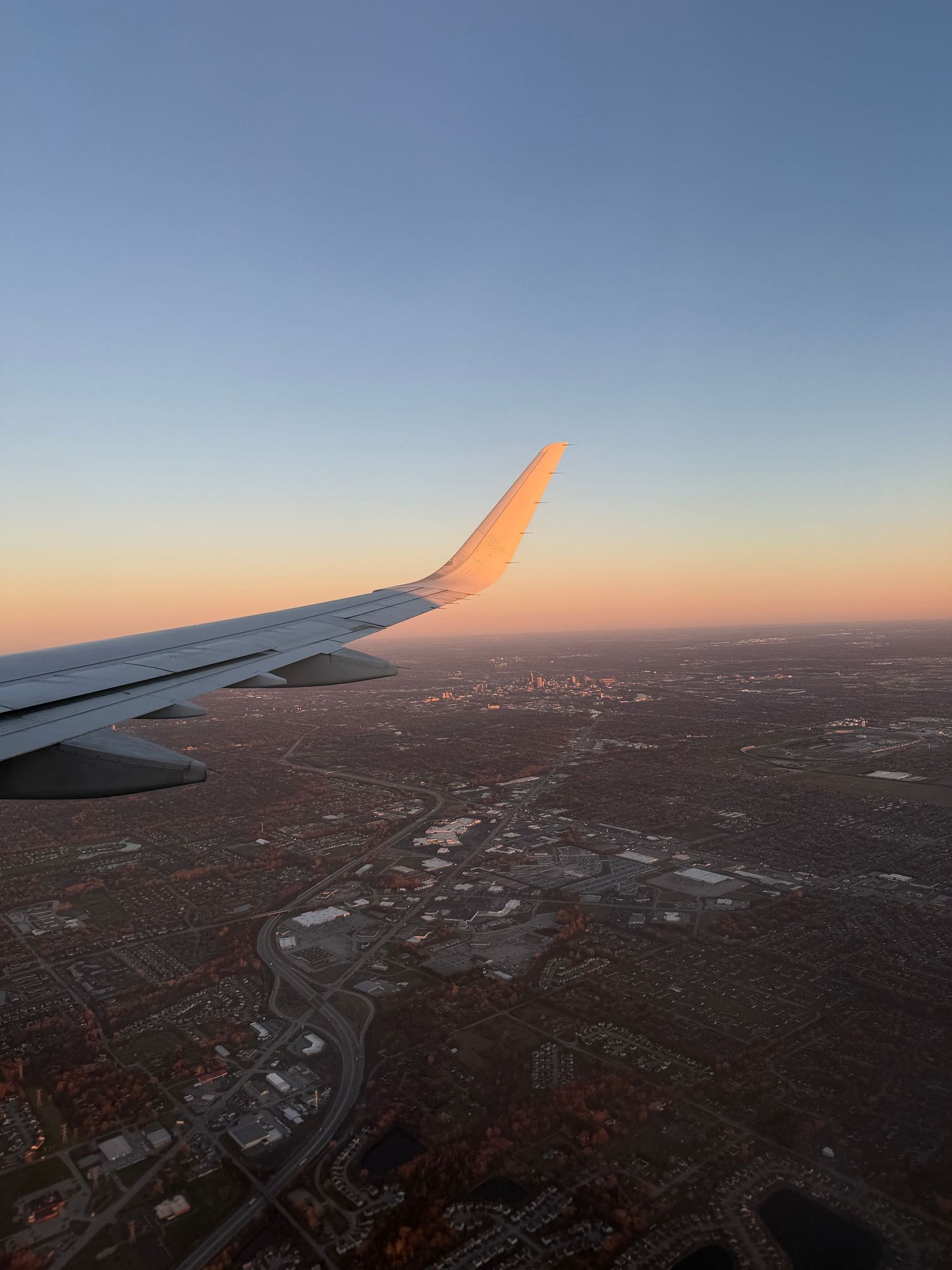 Airplane wing silhouetted against a vibrant orange and pink sunset sky over city Indianapolis senior photographer Regan Nichalson Creative