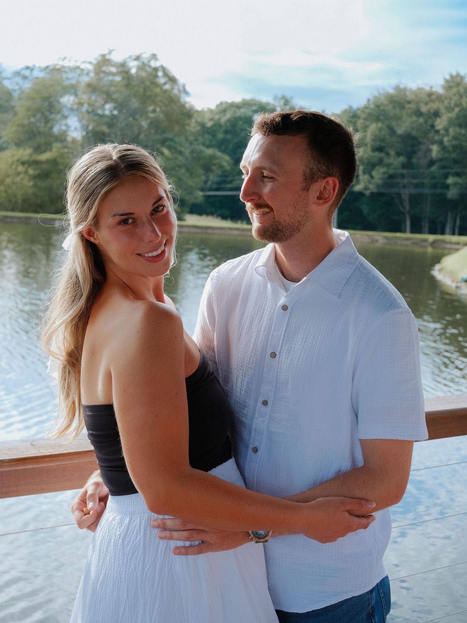 Smiling couple embracing on a sunny wooden deck with a serene lake and trees Hamilton County couples photographer Regan Nichalson Creative