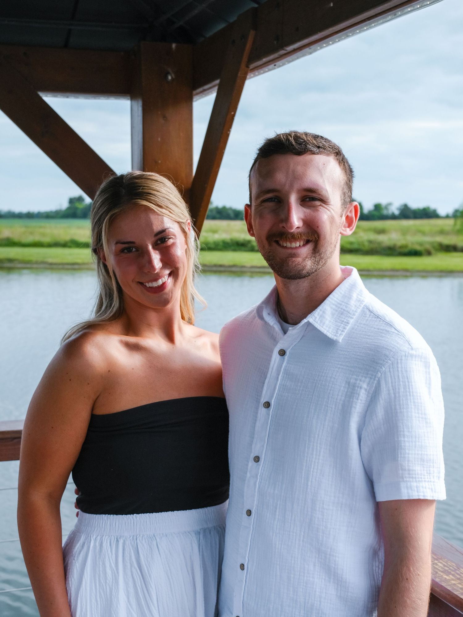 Happy couple posing together under gazebo with scenic lake and green fields Hamilton County couples photographer Regan Nichalson Creative