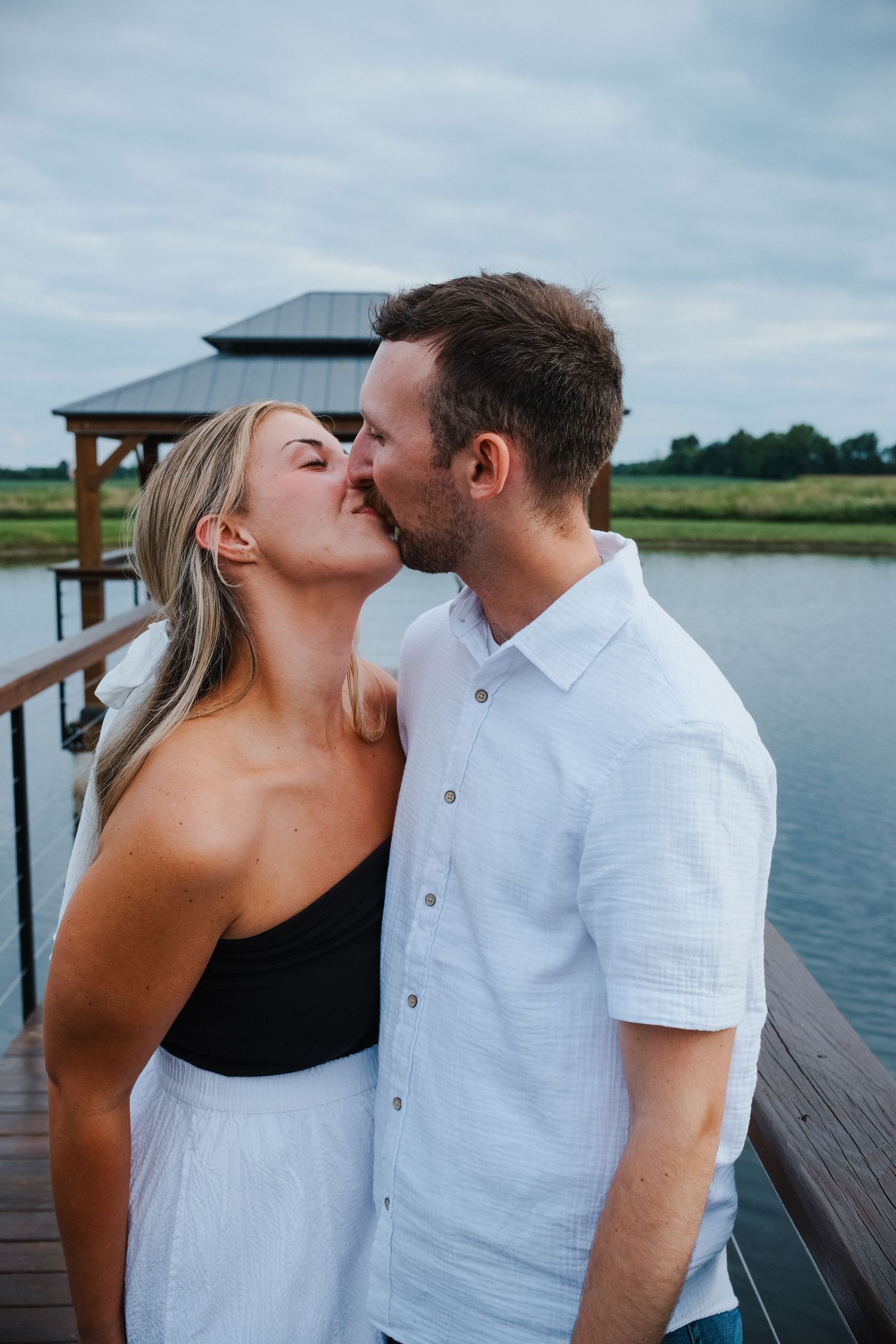 Couple sharing a tender kiss on a wooden dock overlooking a calm lake Hamilton County couples photographer Regan Nichalson Creative