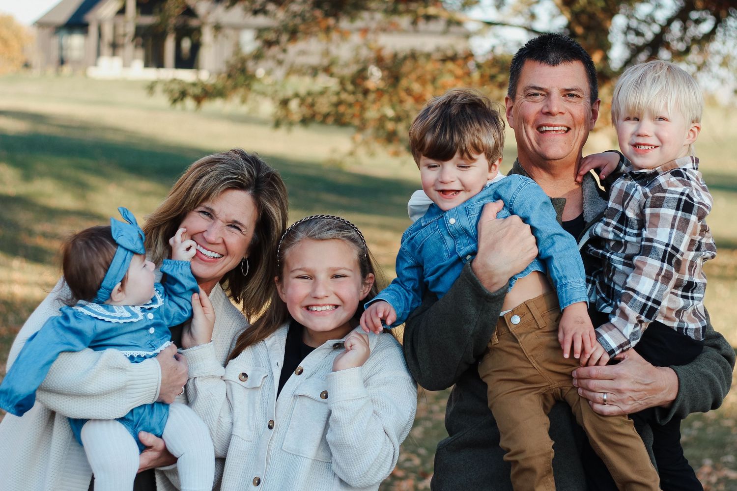 Happy family of six posing outdoors in autumn with parents holding three young children Zionsville family photographer Regan Nichalson Creat