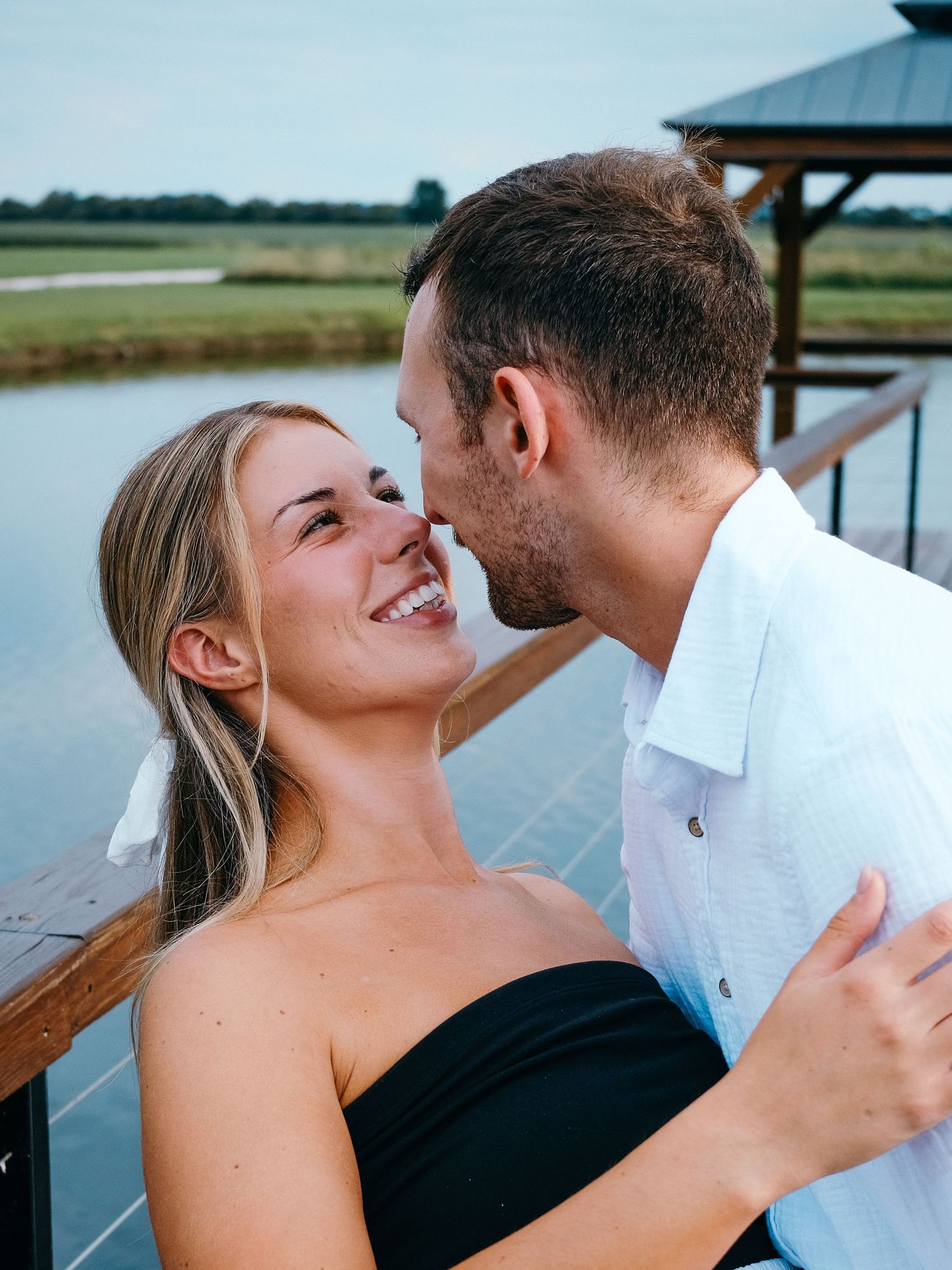 Smiling blonde woman in black strapless top being kissed by man on waterfront Hamilton County couples photographer Regan Nichalson Creative