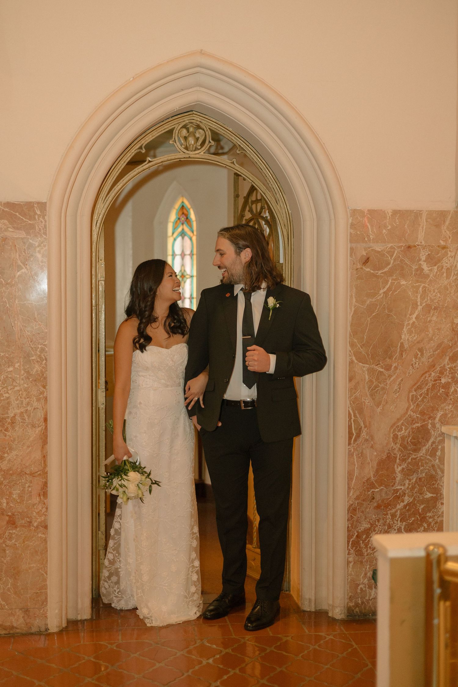 A couple shares intimate moments in an ornate church archway with marble walls.