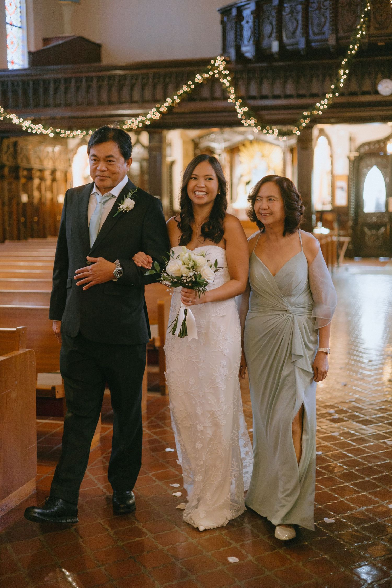 Wedding party walking down church aisle decorated with holiday lights and traditional decor.
