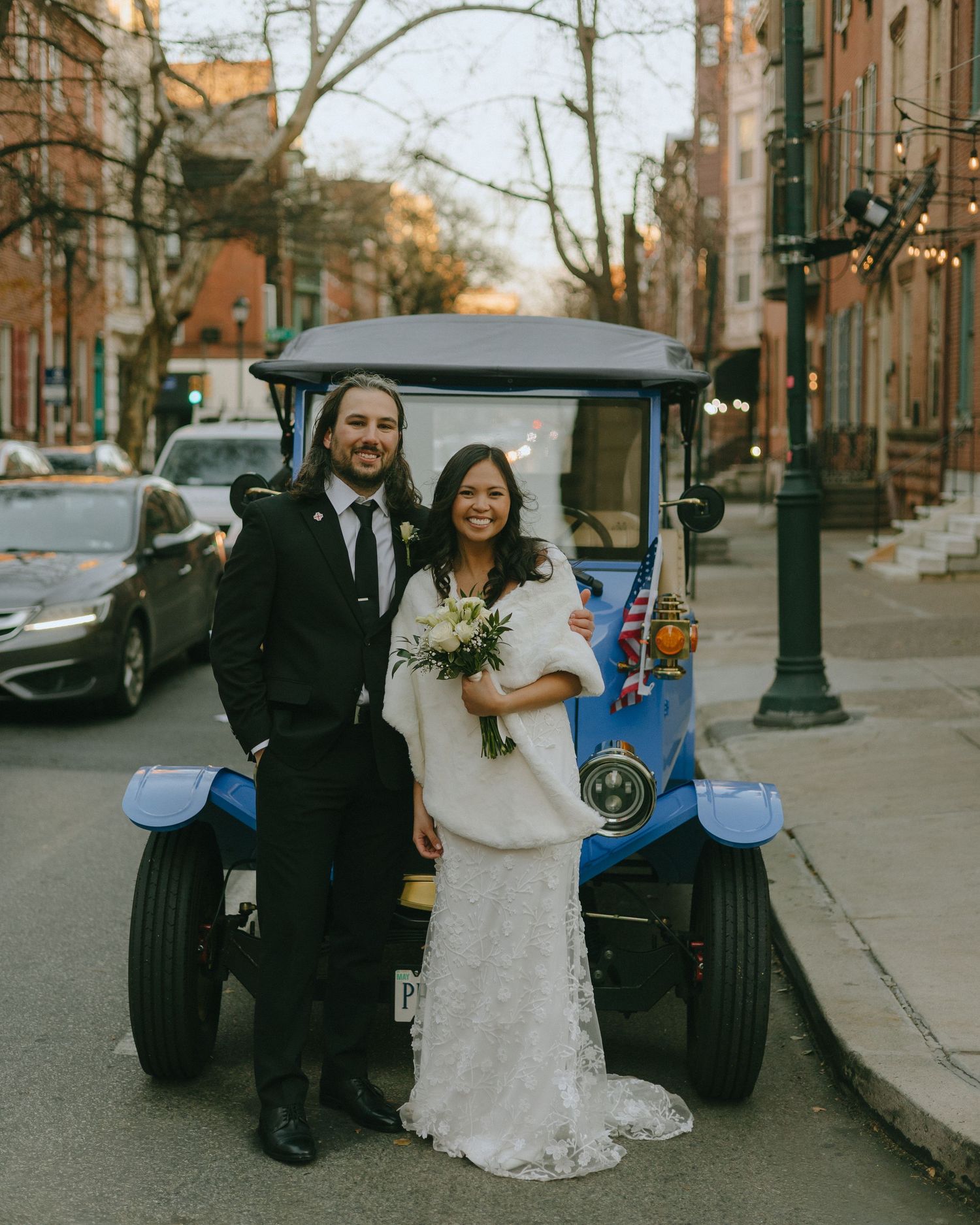 Wedding couple poses with vintage blue golf cart on a city street.