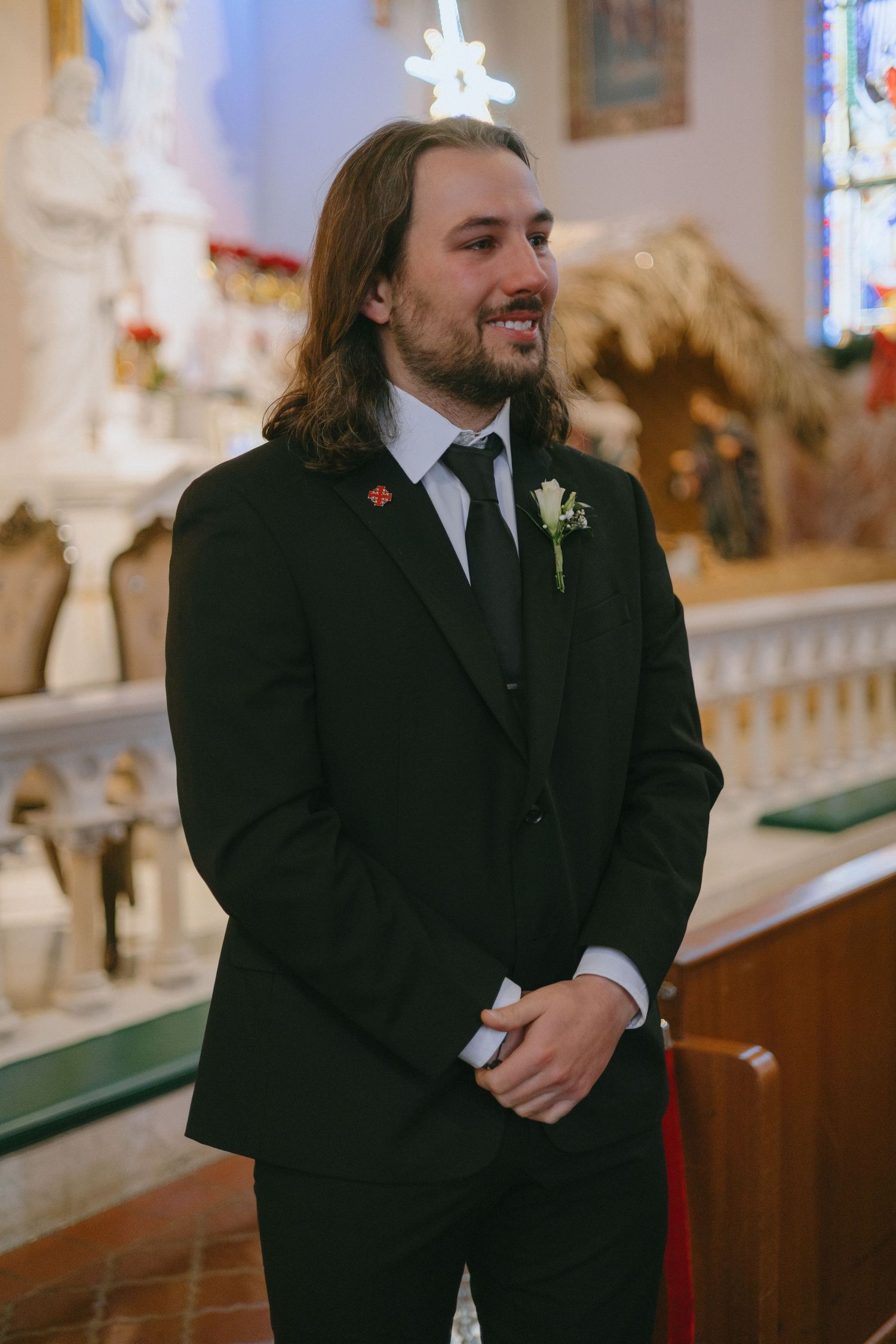 A groom smiles with joy during wedding ceremony in front of church altar.