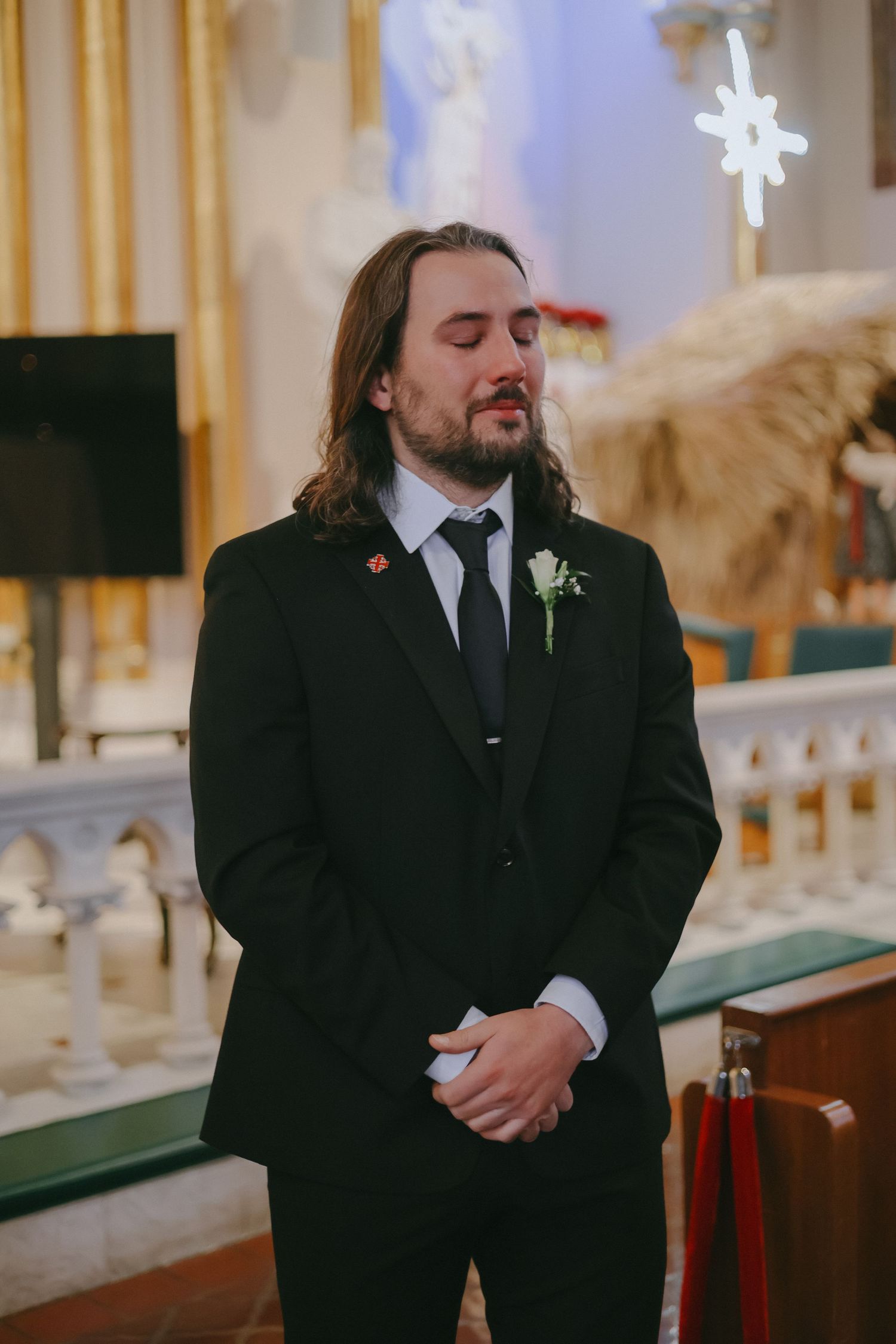 A groom stands in a traditional church setting with decorative altar and stained glass windows.