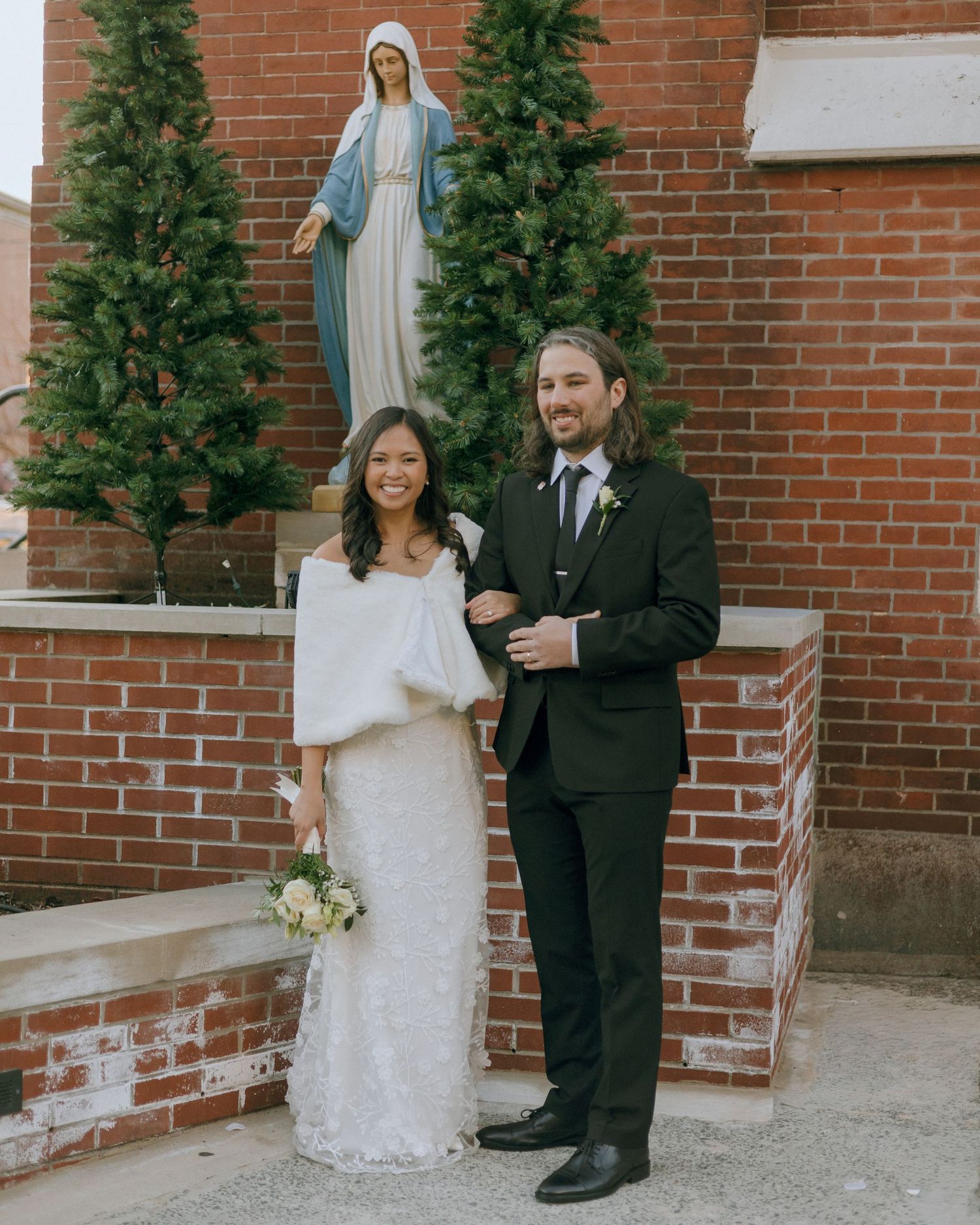 Newlyweds pose for portraits against a red brick wall with greenery.