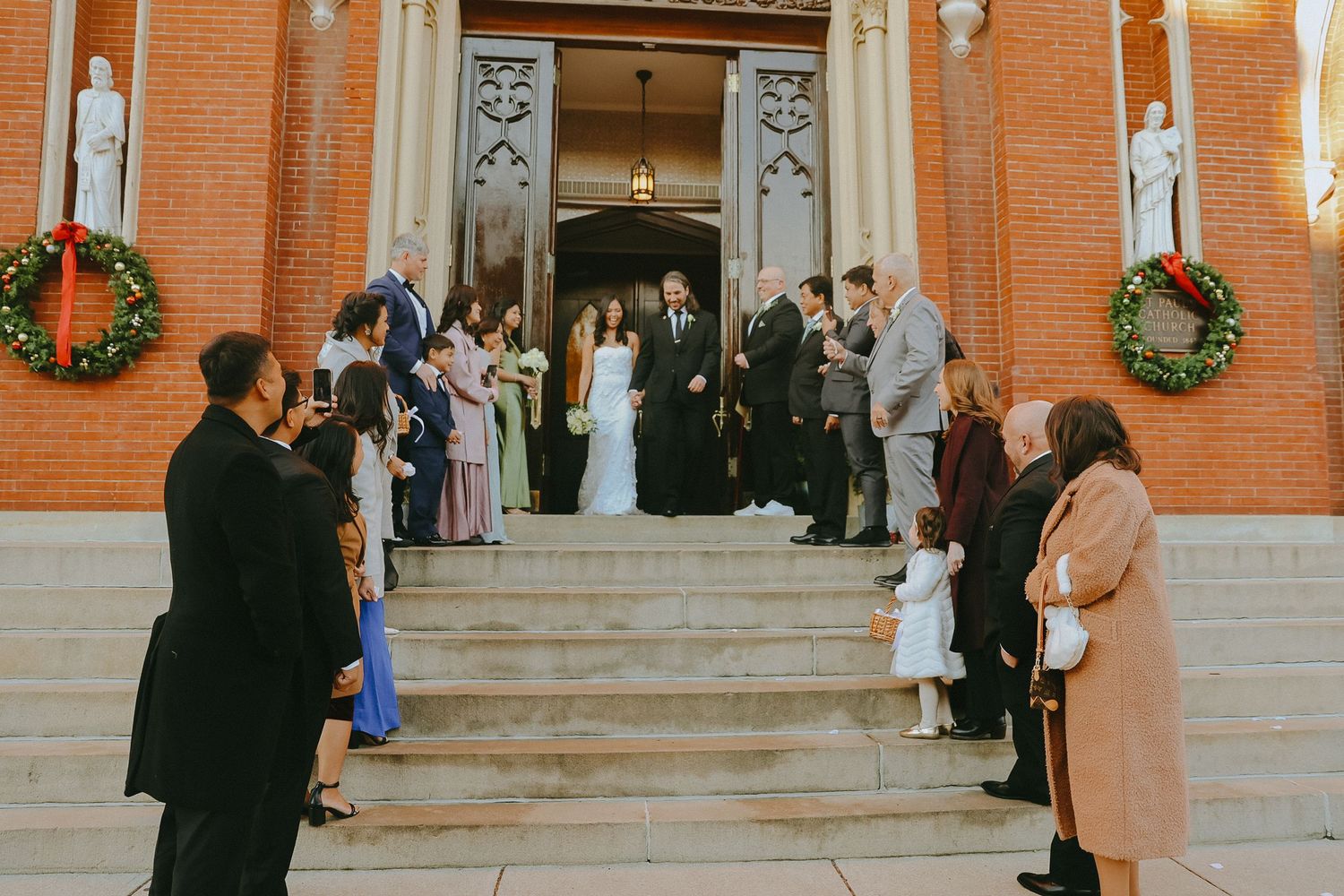 Wedding guests gathering outside brick church entrance with holiday wreaths.