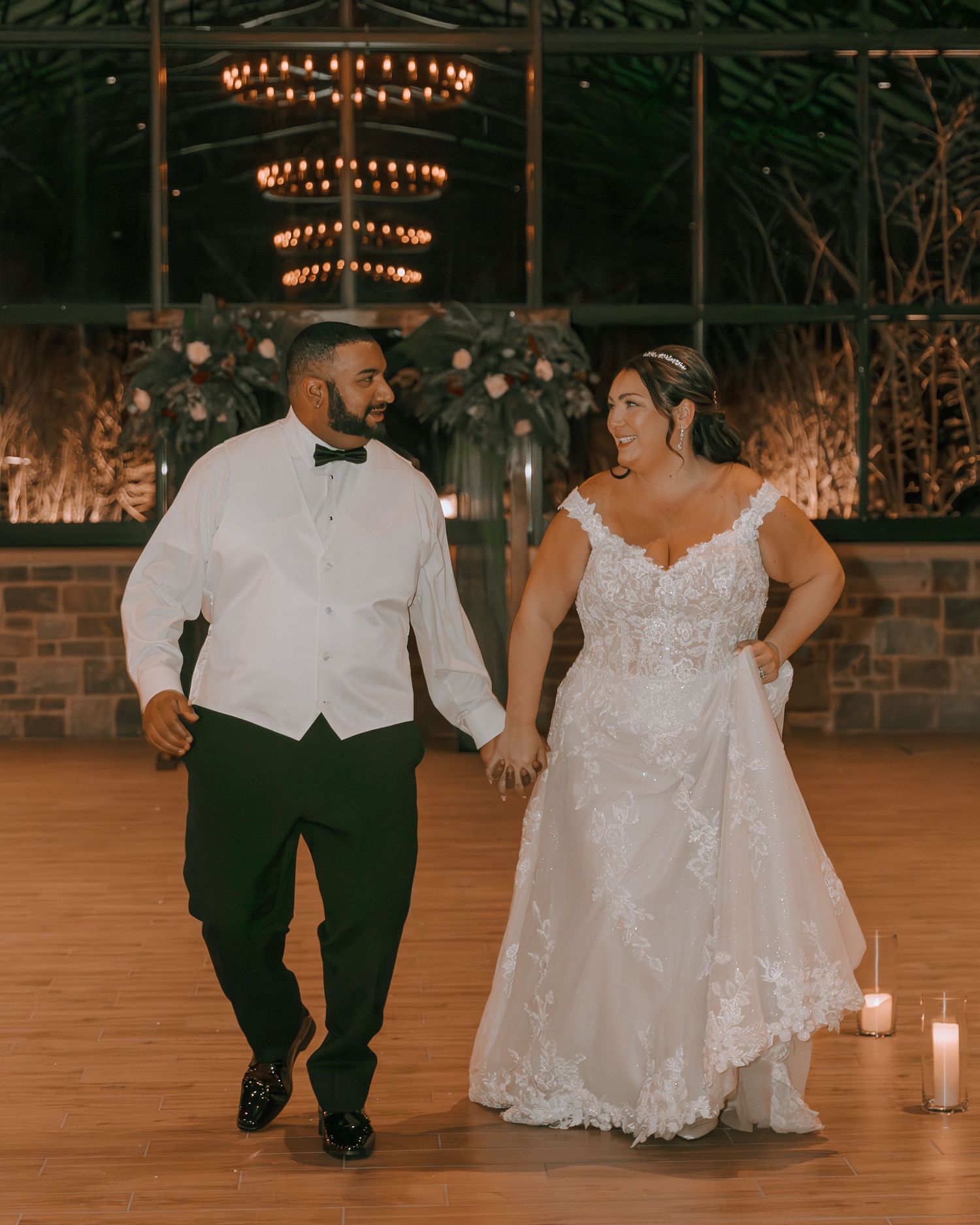 A couple dances together at their wedding reception under elegant chandeliers in a rustic venue.
