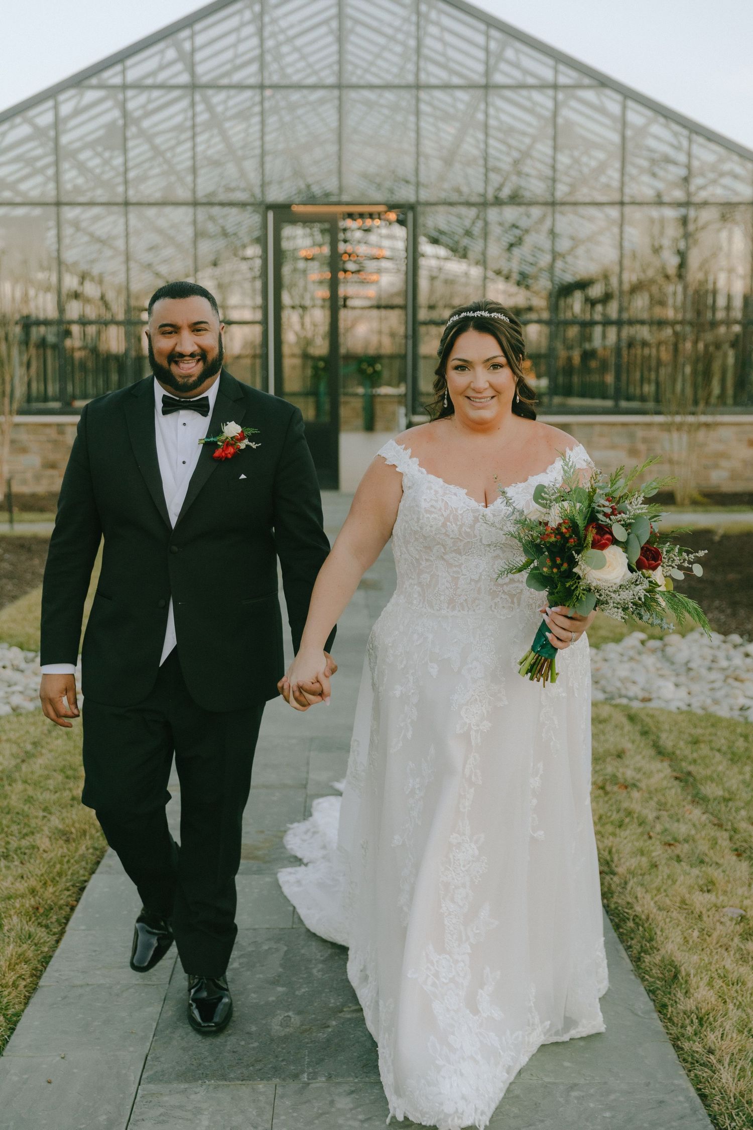 A happy couple walks hand in hand outside a glass greenhouse wedding venue.